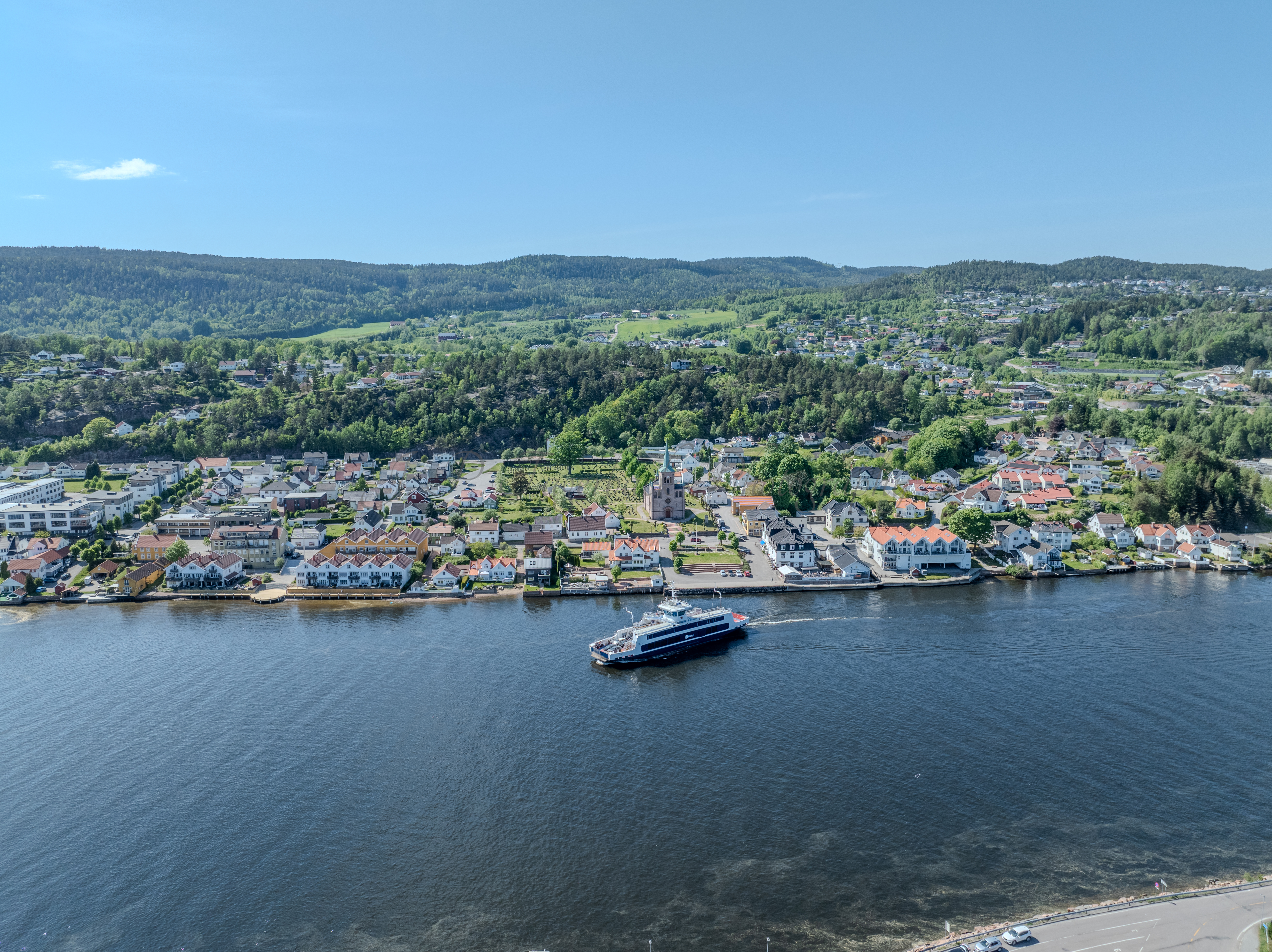 Buildings on both sides of a fjord where a ferry and other smaller boats are sailing