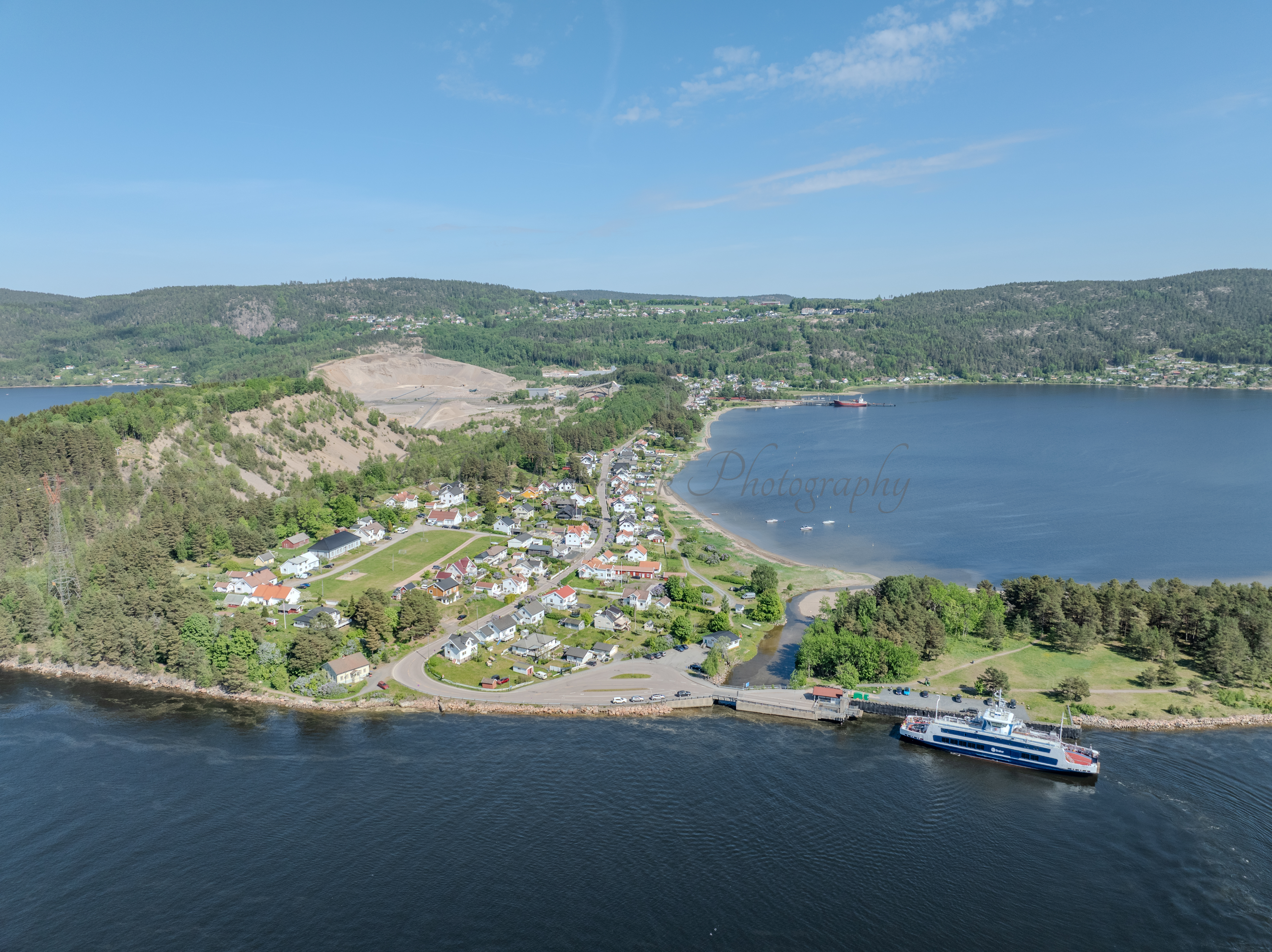 Buildings on both sides of a fjord where a ferry and other smaller boats are sailing