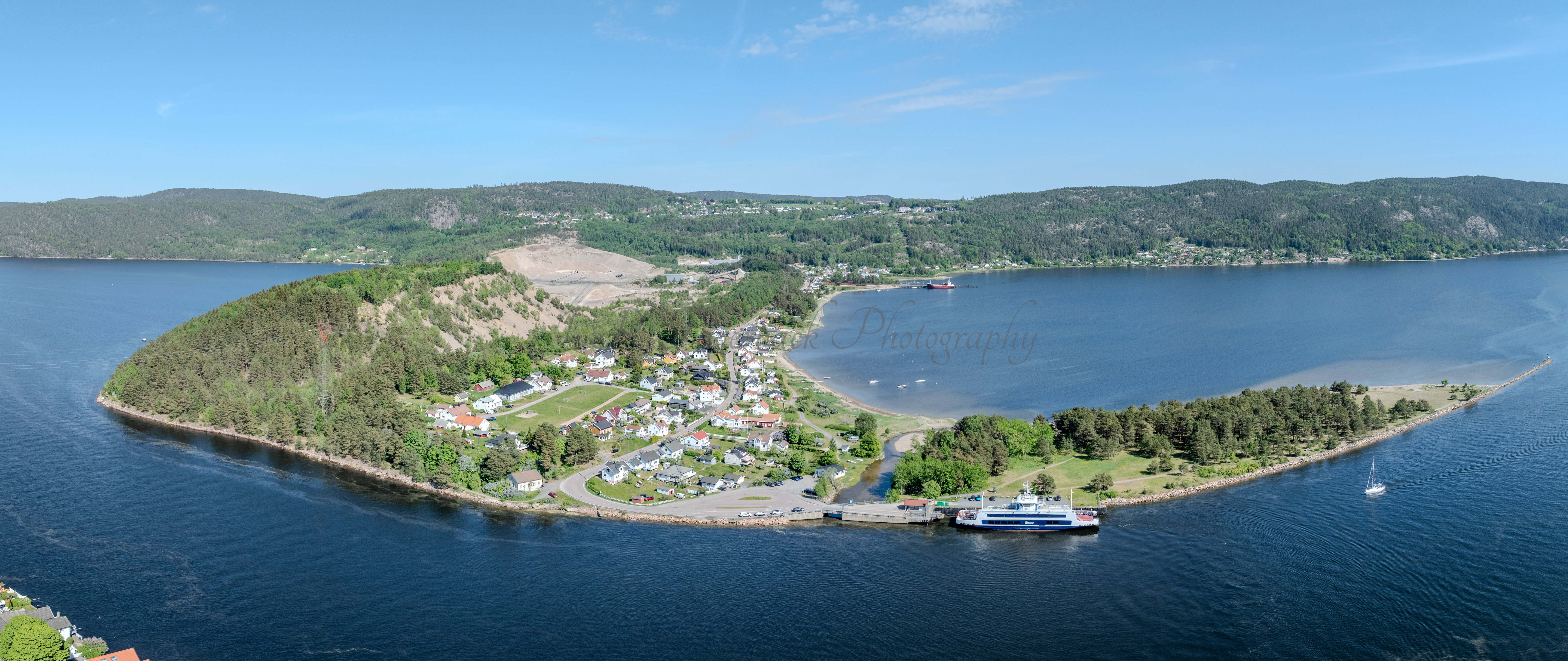 Buildings on both sides of a fjord where a ferry and other smaller boats are sailing