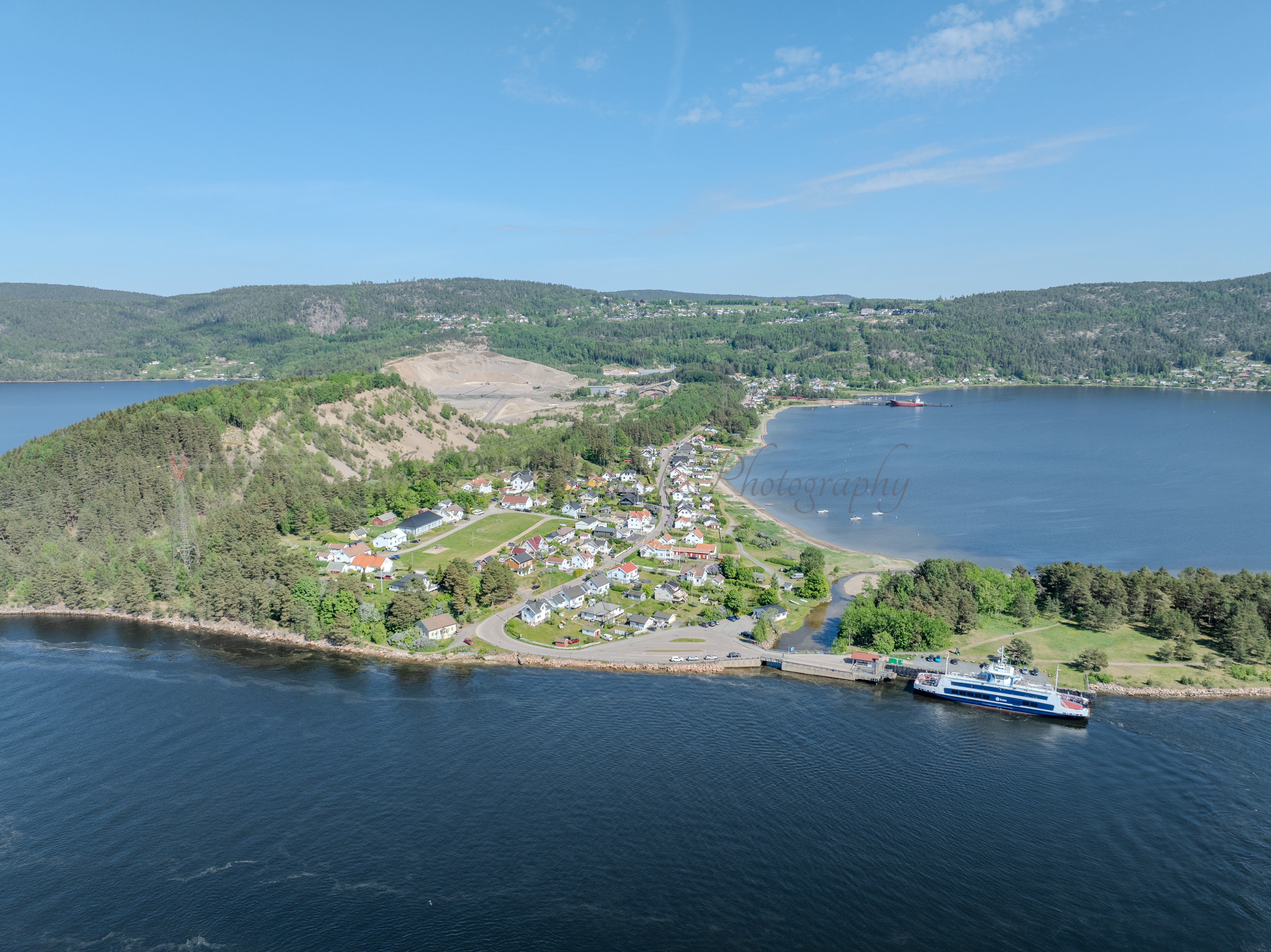 Buildings on both sides of a fjord where a ferry and other smaller boats are sailing