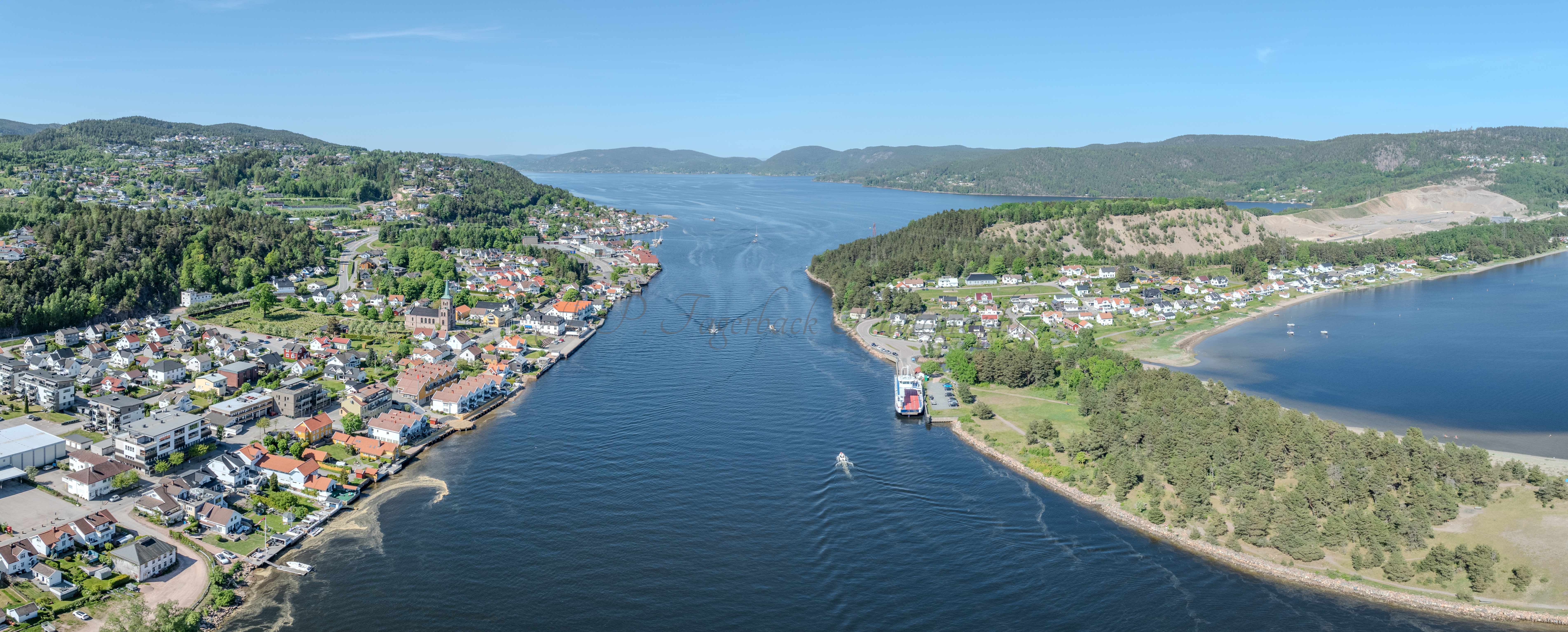Buildings on both sides of a fjord where a ferry and other smaller boats are sailing