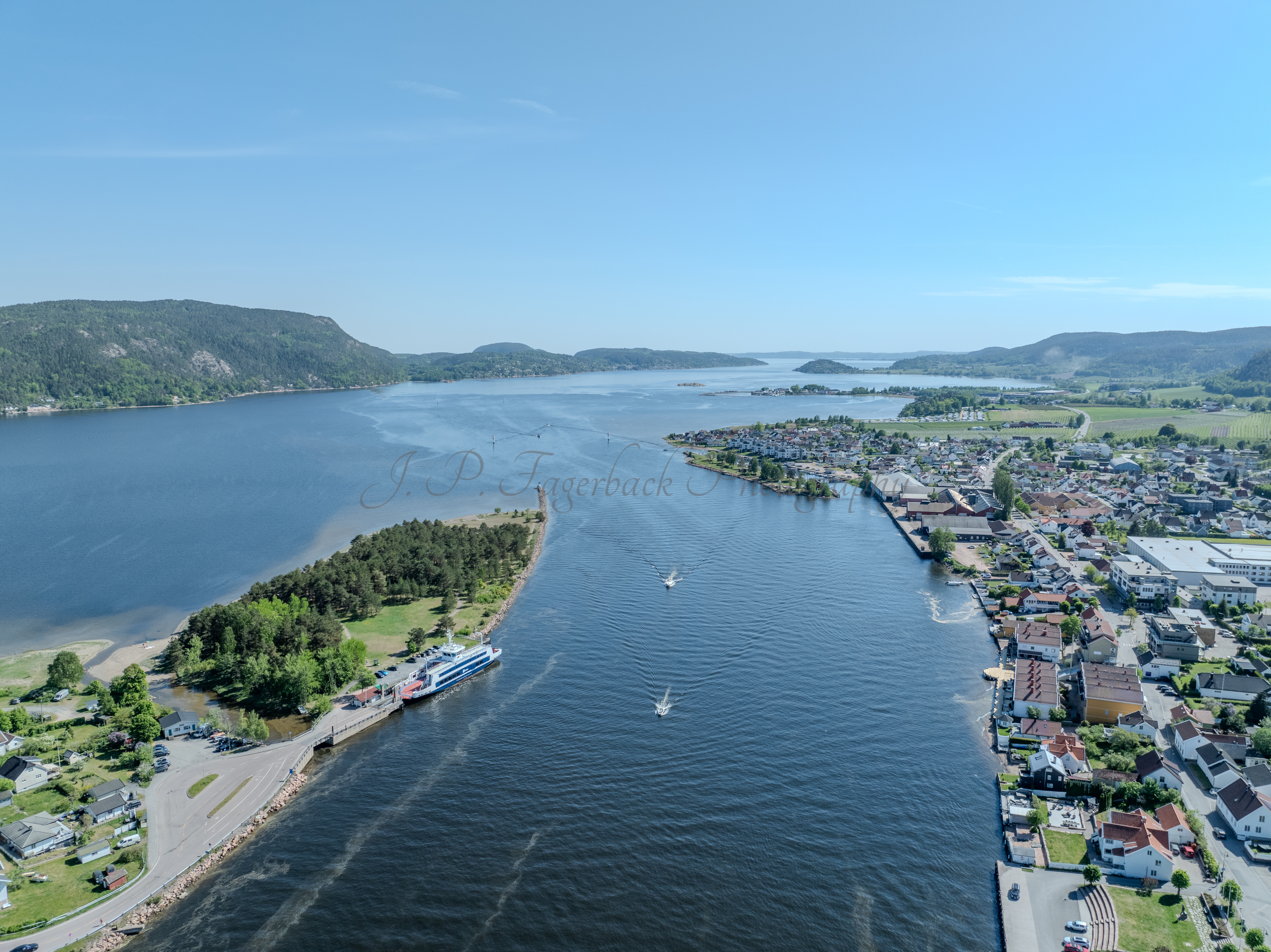 Buildings on both sides of a fjord where a ferry and other smaller boats are sailing