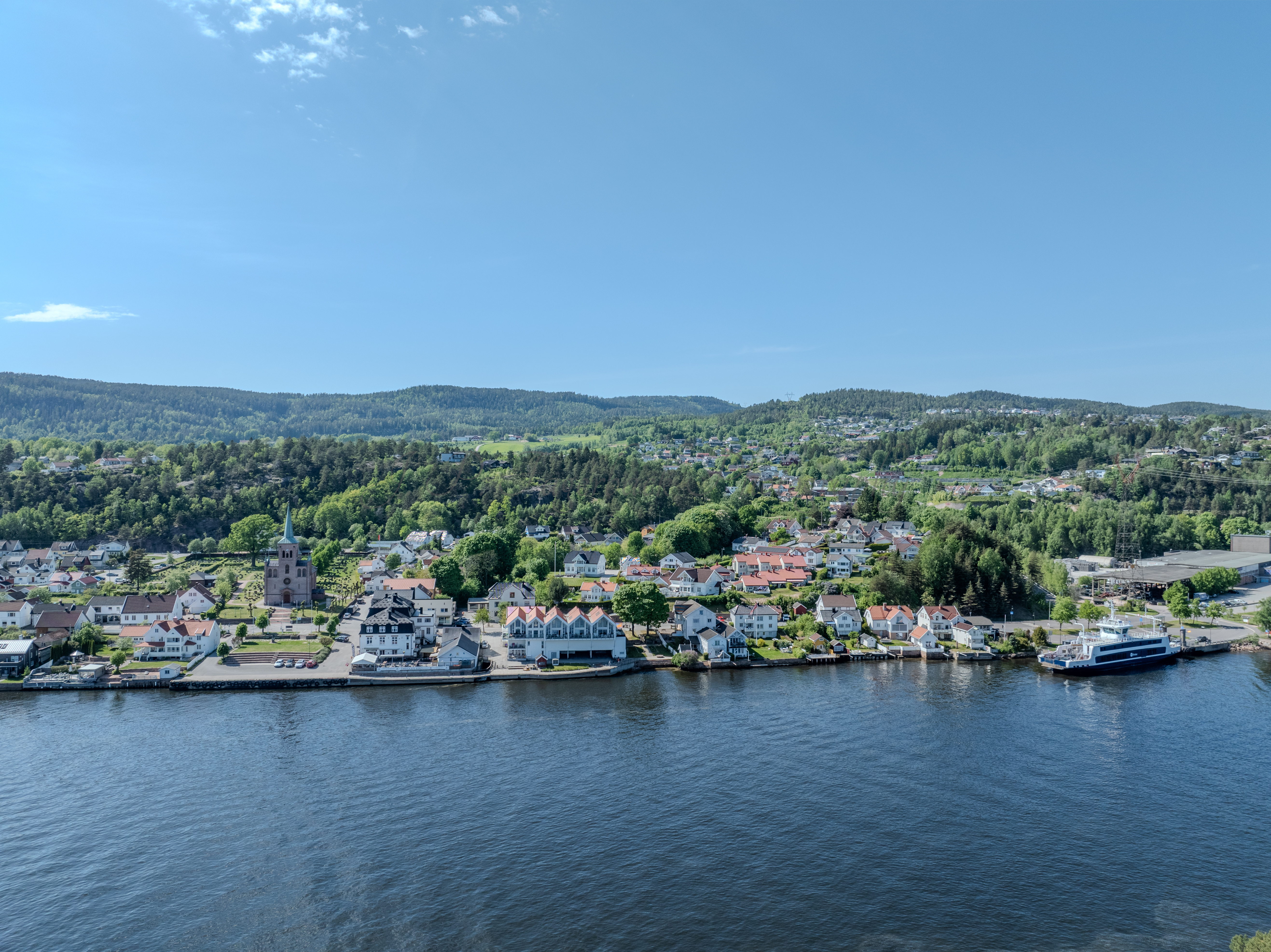 Buildings on both sides of a fjord where a ferry and other smaller boats are sailing
