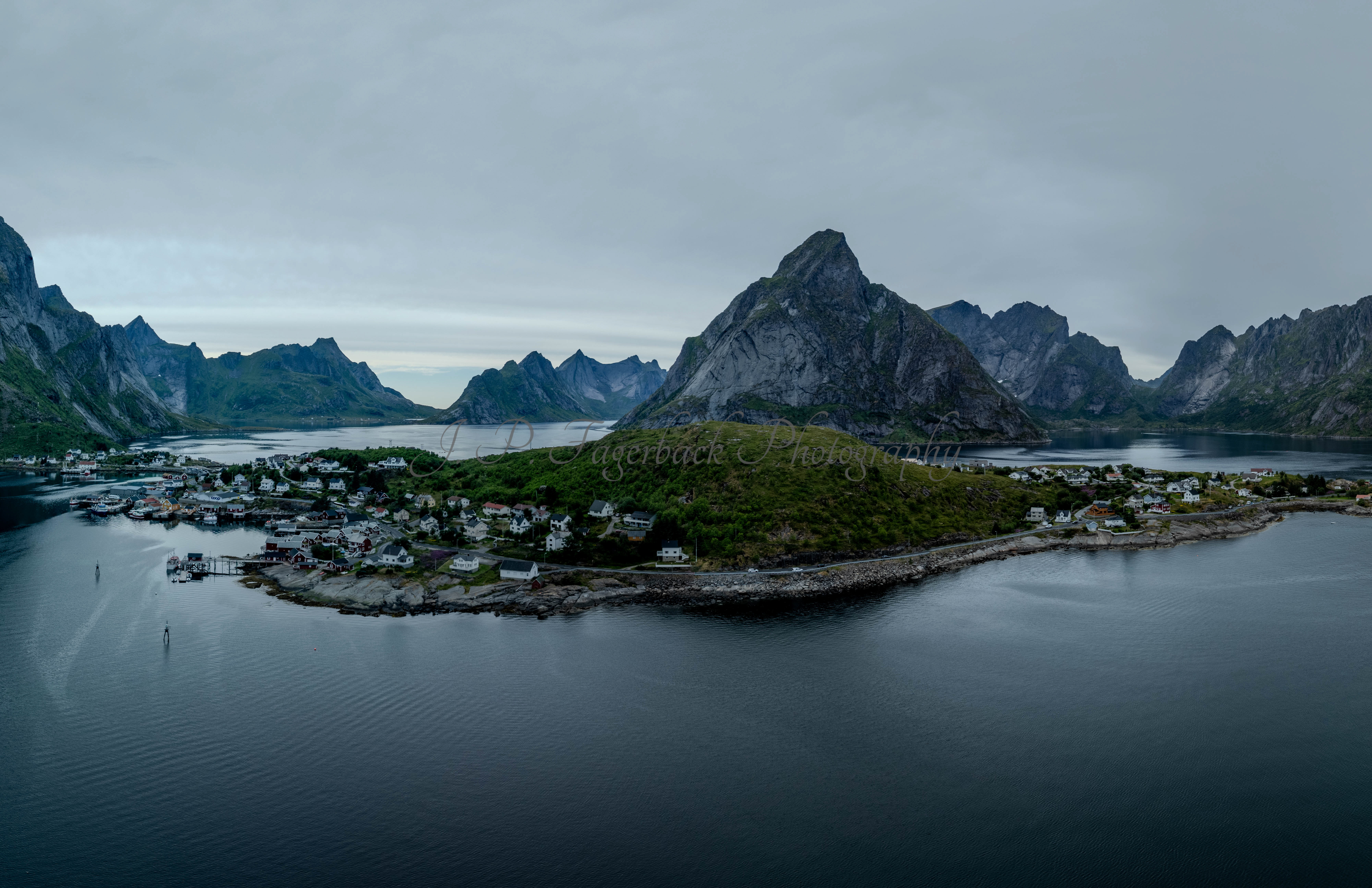 Buildings along the shore of a body of water with a mountain in the background on a gray day