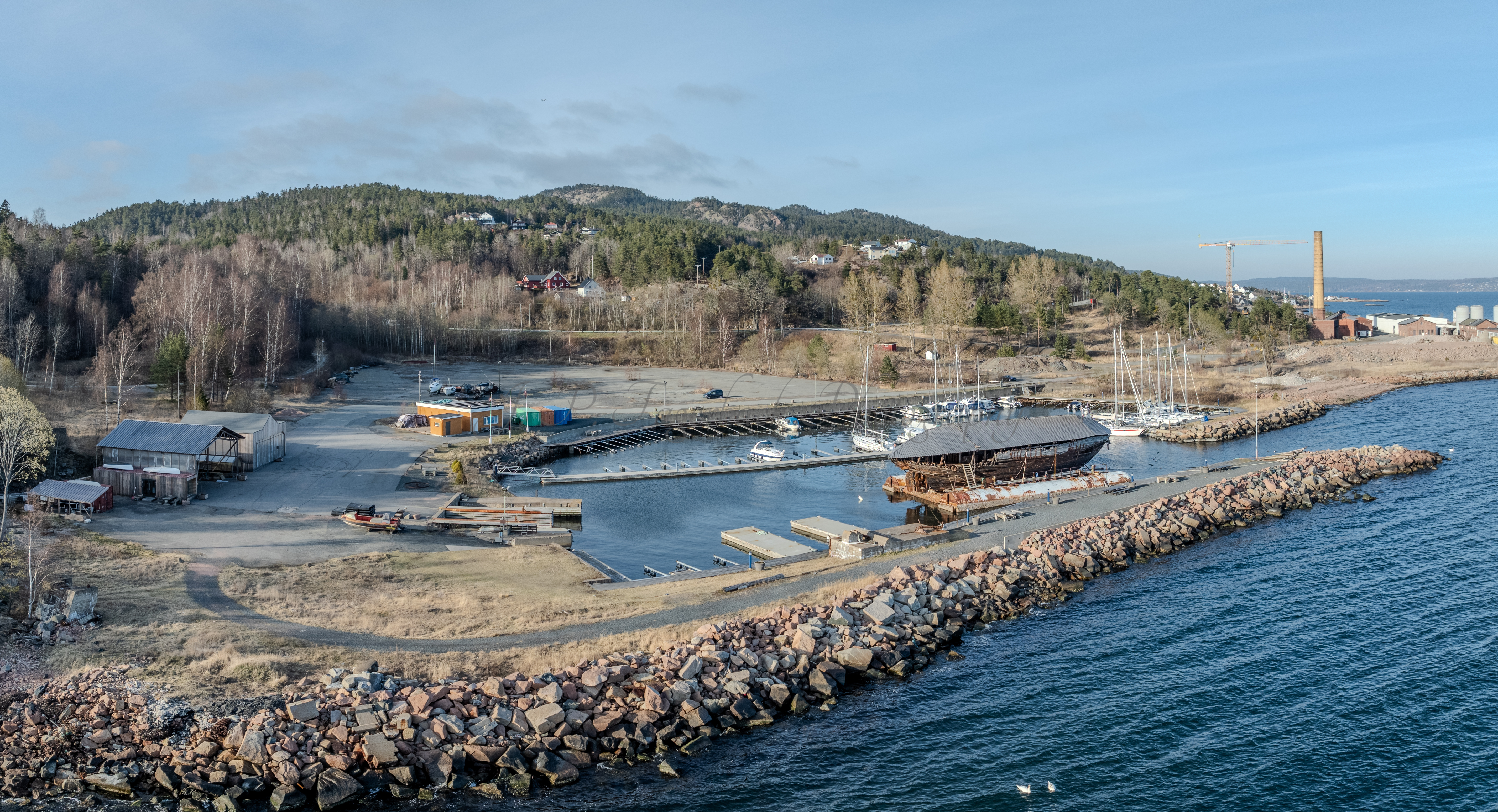 An old ship  wreck with a protection roof over it in a marina by a large body of water under a blue sky