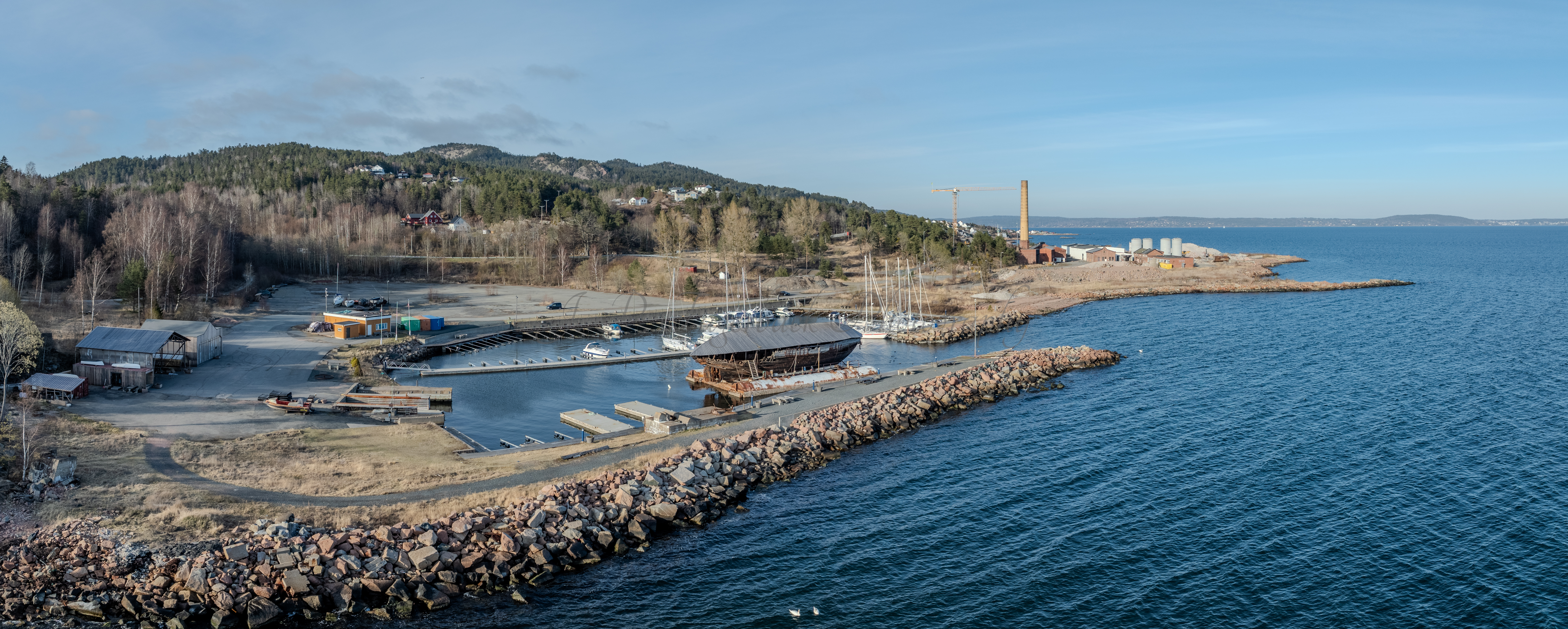 An old ship  wreck with a protection roof over it in a marina by a large body of water under a blue sky