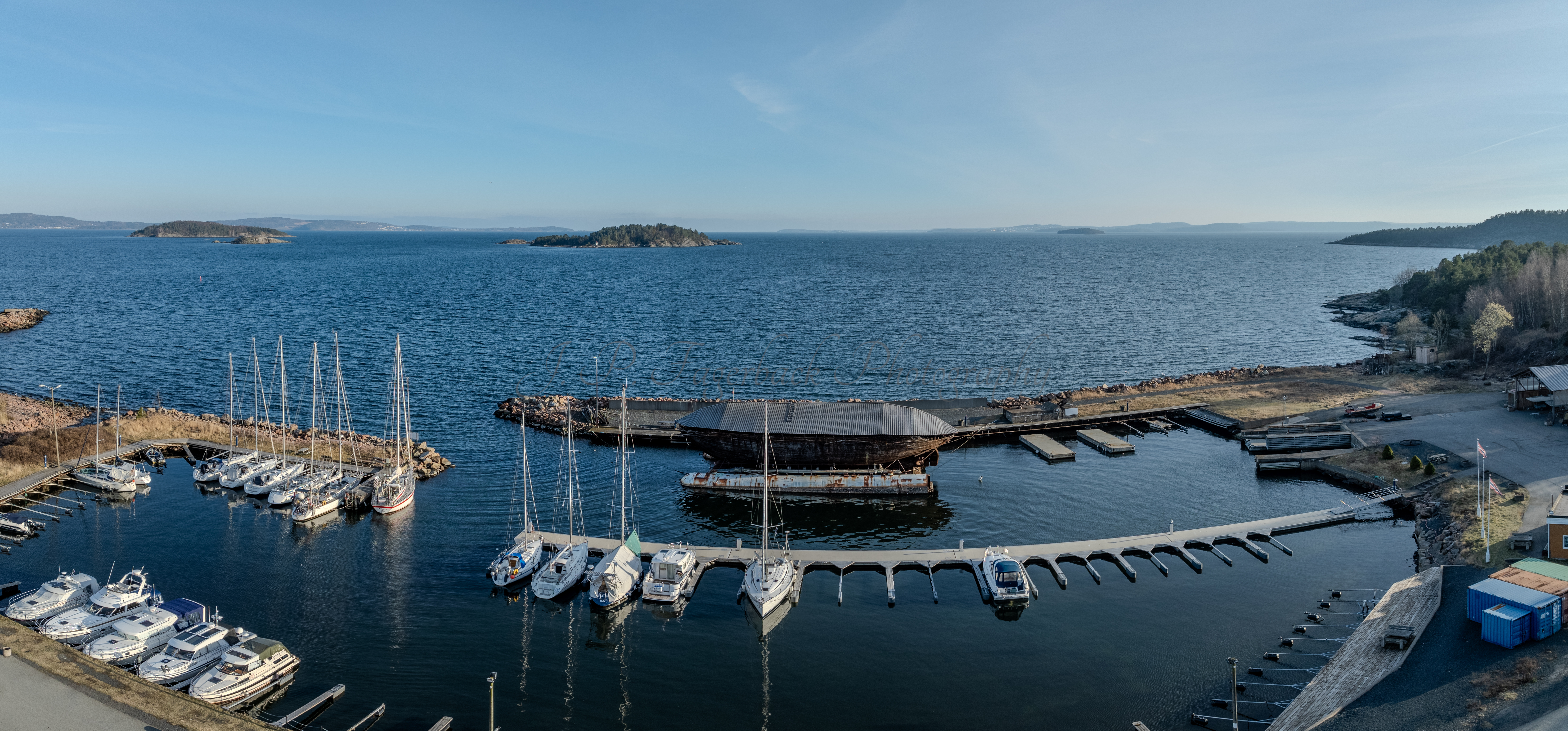 An old ship  wreck with a protection roof over it in a marina by a large body of water under a blue sky