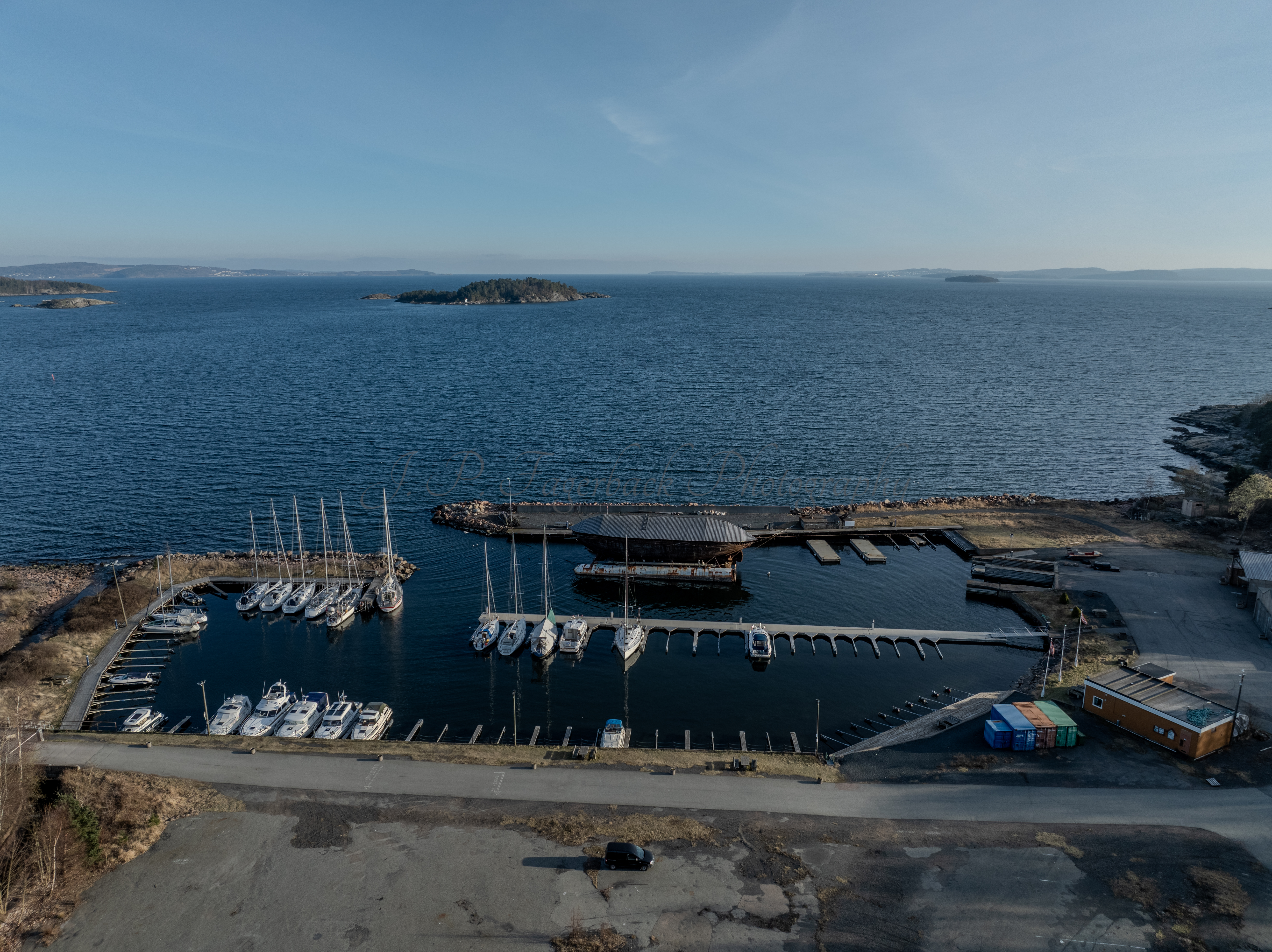 An old ship  wreck with a protection roof over it in a marina by a large body of water under a blue sky