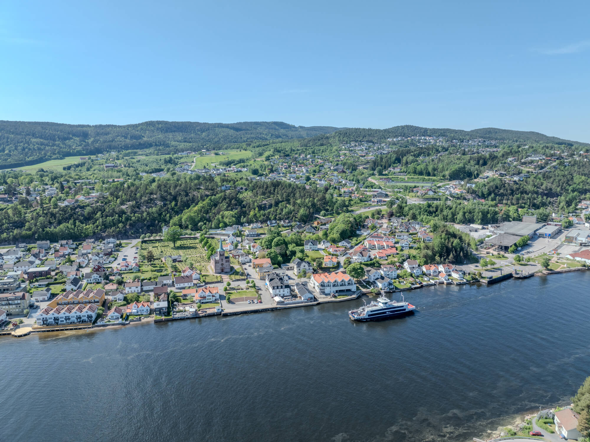 Buildings on both sides of a fjord where a ferry and other smaller boats are sailing