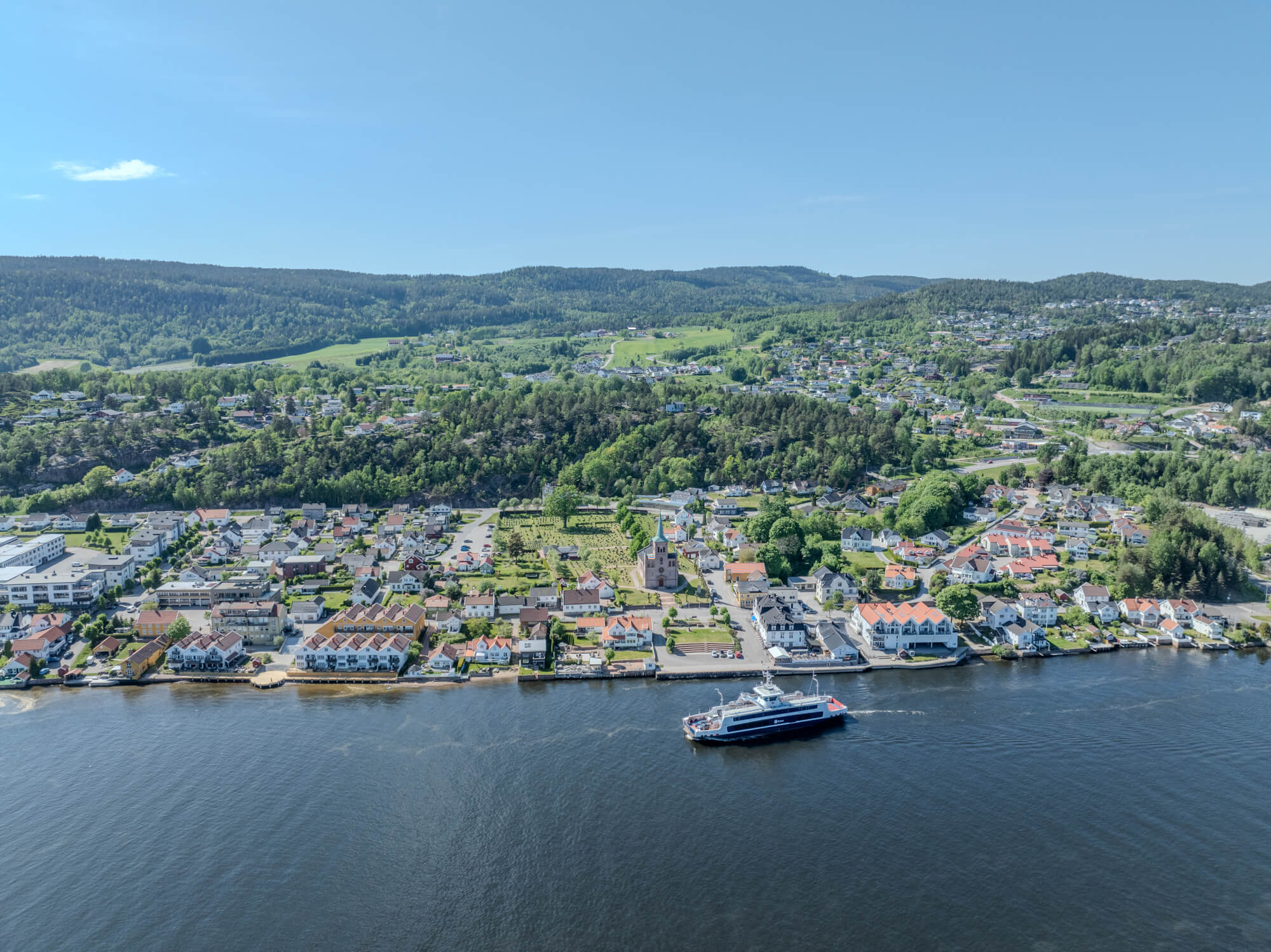 Buildings on both sides of a fjord where a ferry and other smaller boats are sailing