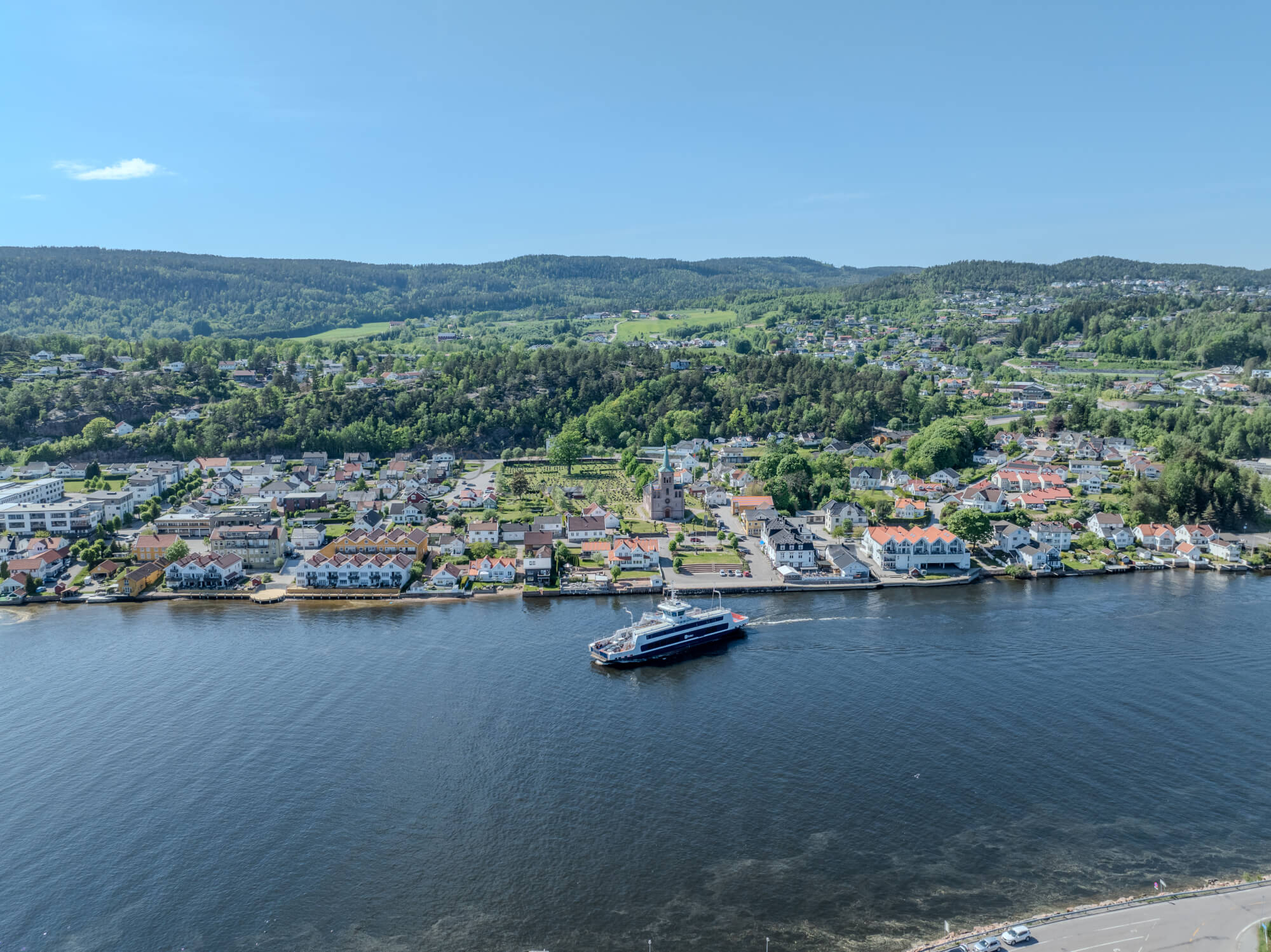 Buildings on both sides of a fjord where a ferry and other smaller boats are sailing