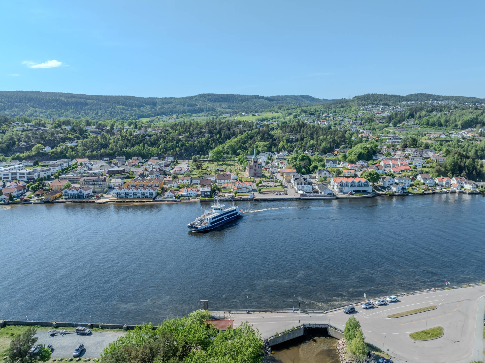 Buildings on both sides of a fjord where a ferry and other smaller boats are sailing