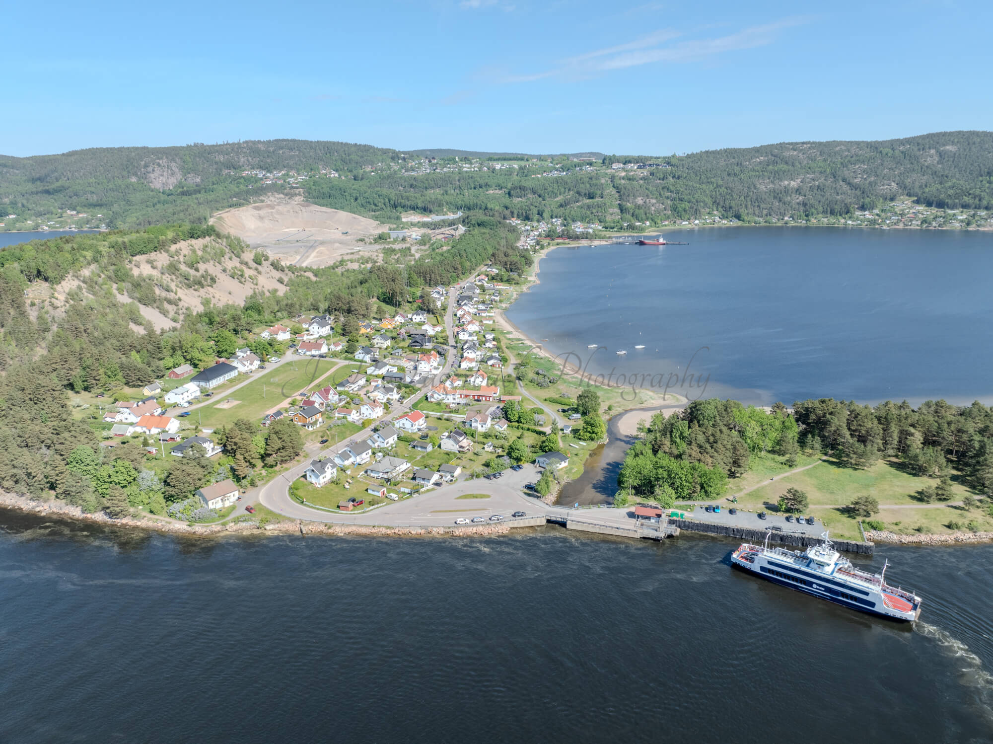 Buildings on both sides of a fjord where a ferry and other smaller boats are sailing