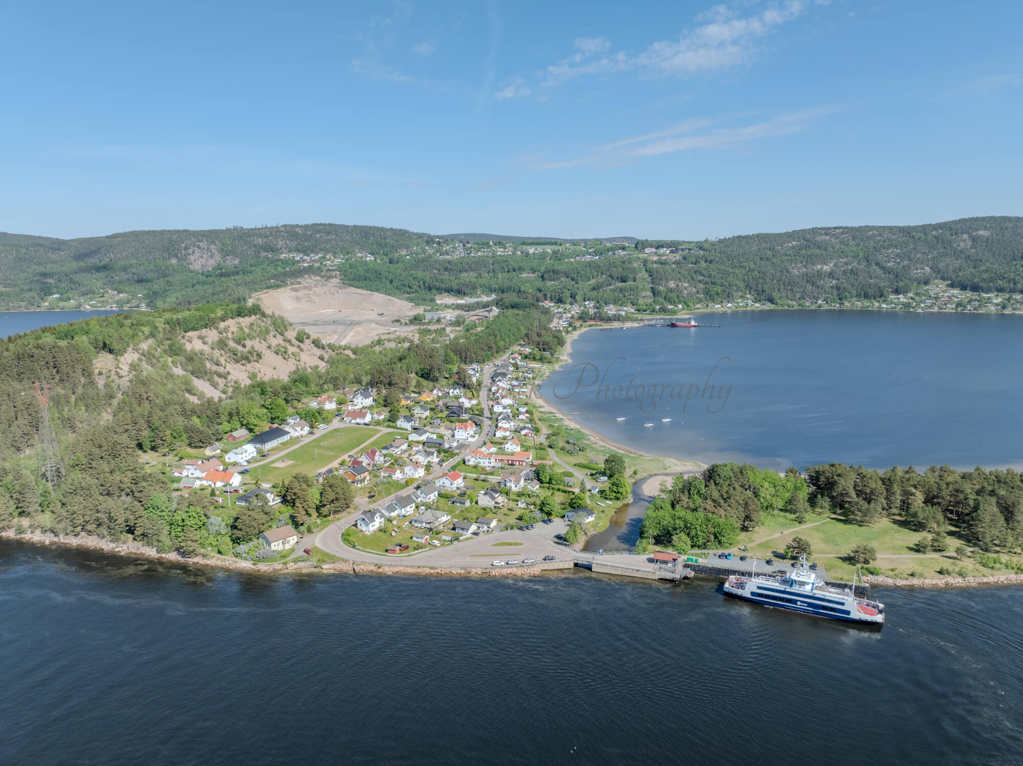 Buildings on both sides of a fjord where a ferry and other smaller boats are sailing