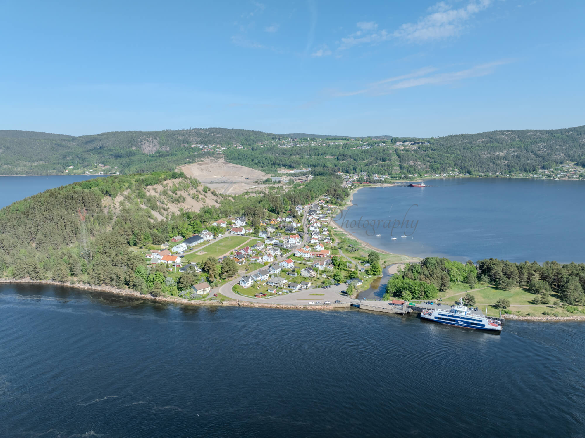 Buildings on both sides of a fjord where a ferry and other smaller boats are sailing
