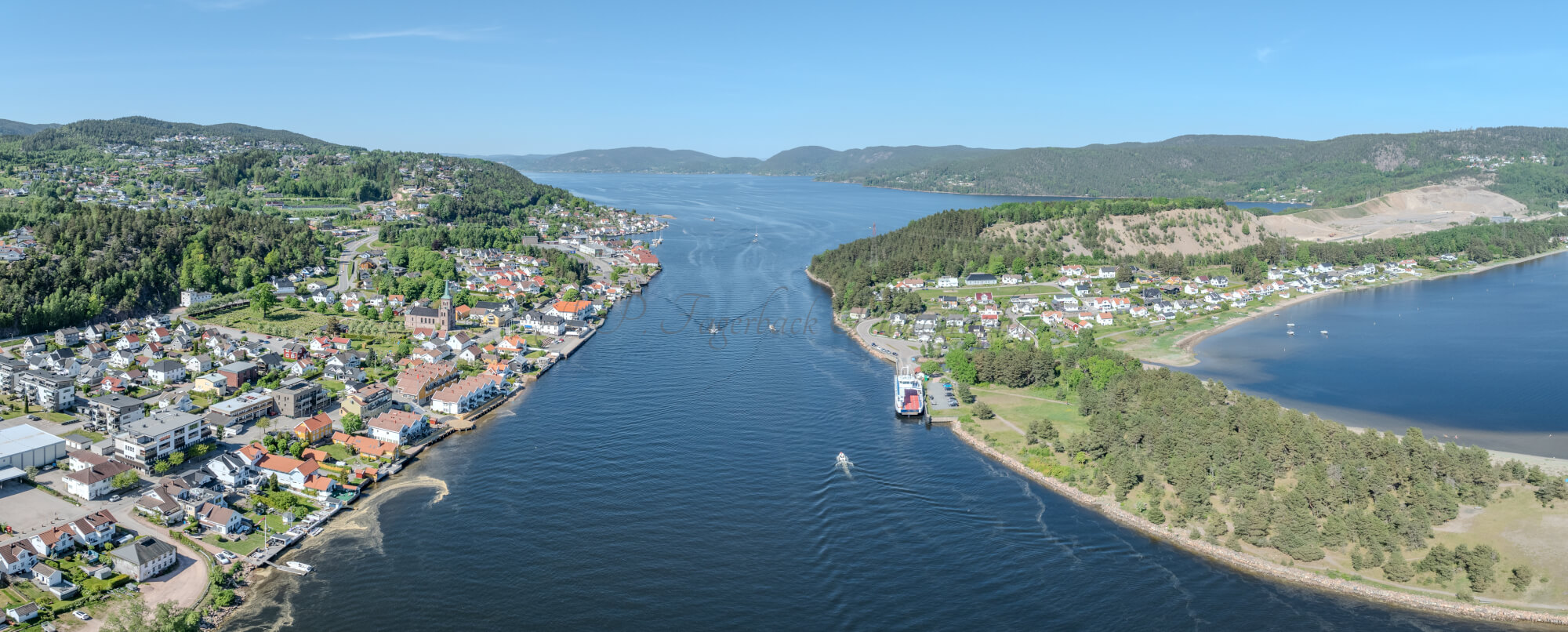 Buildings on both sides of a fjord where a ferry and other smaller boats are sailing