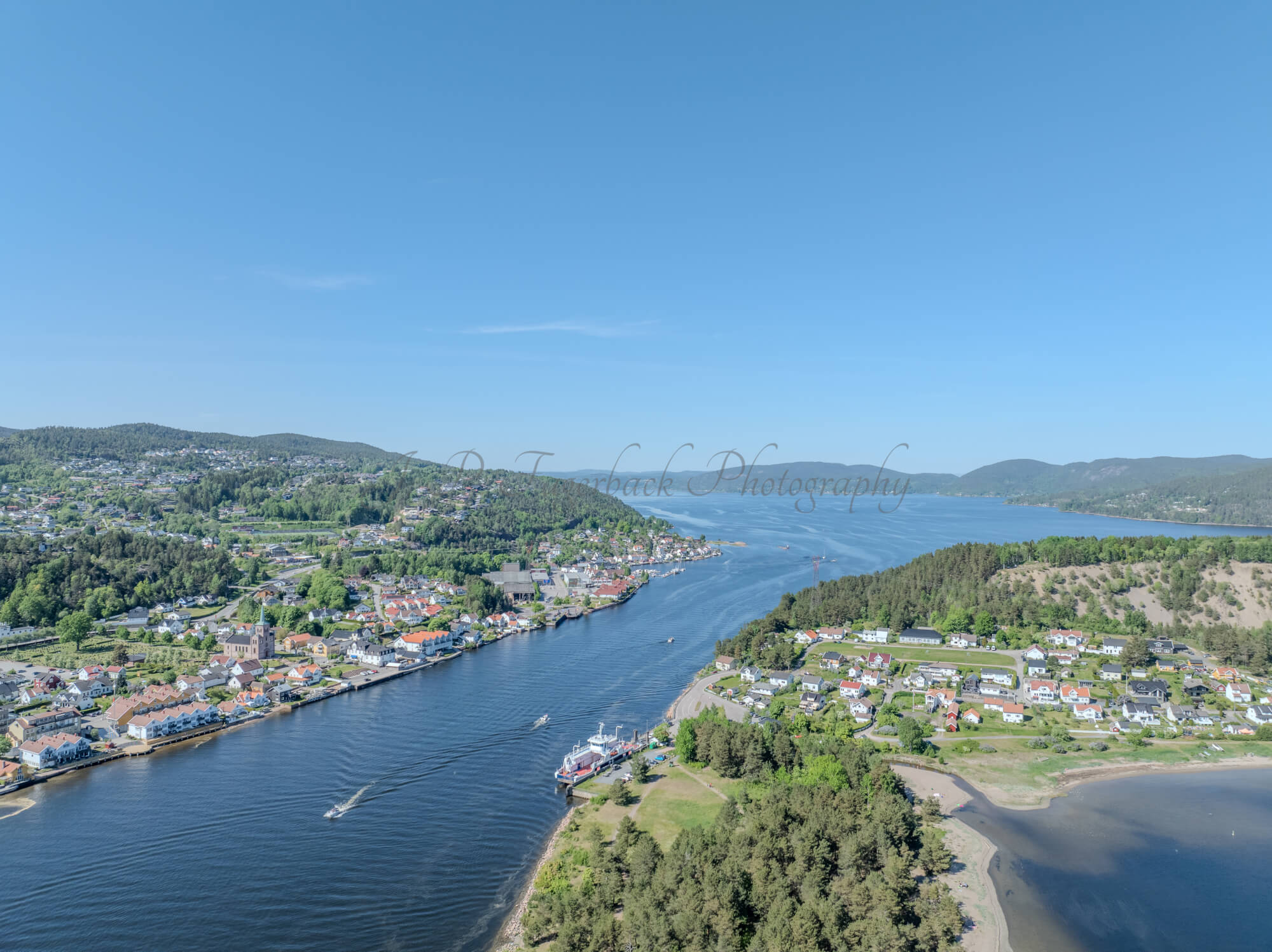 Buildings on both sides of a fjord where a ferry and other smaller boats are sailing
