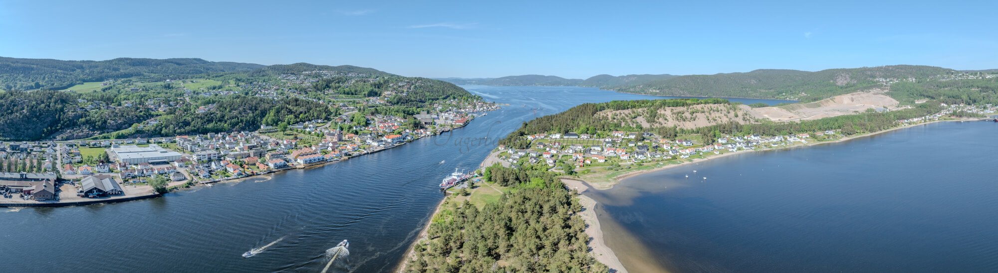 Buildings on both sides of a fjord where a ferry and other smaller boats are sailing