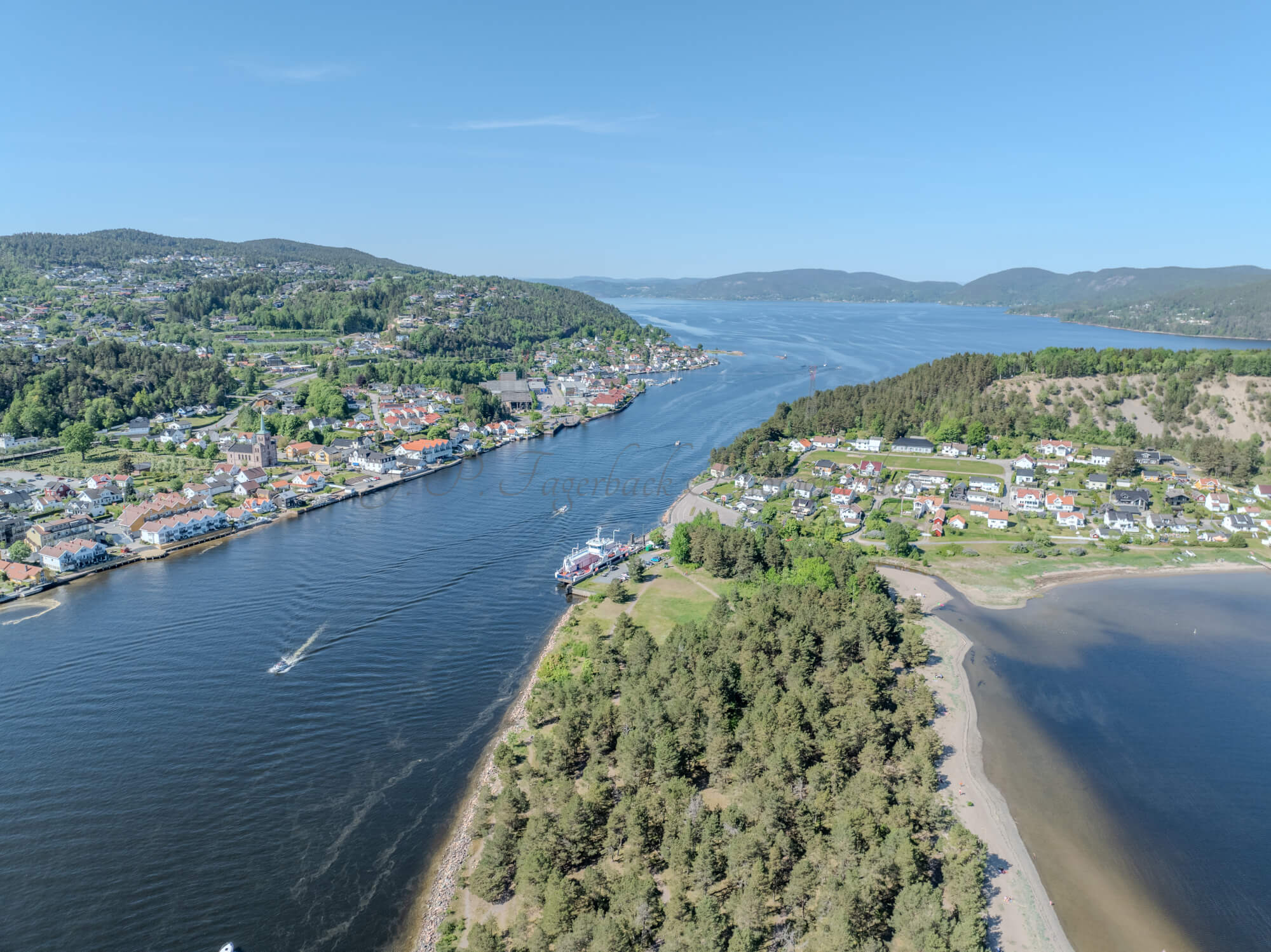 Buildings on both sides of a fjord where a ferry and other smaller boats are sailing