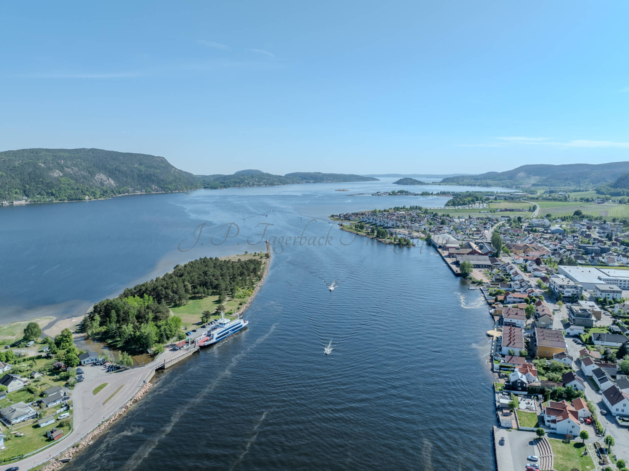Buildings on both sides of a fjord where a ferry and other smaller boats are sailing