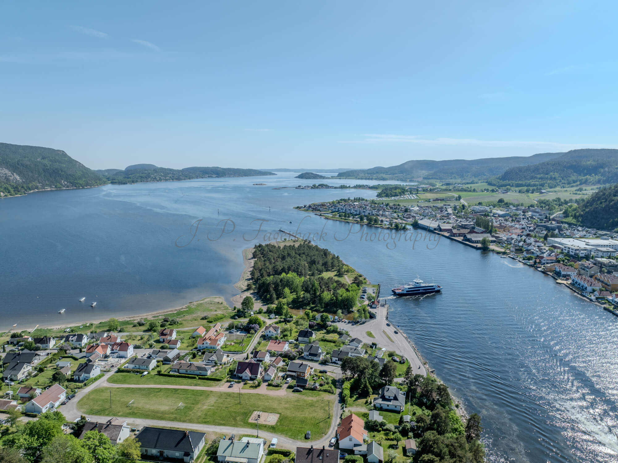 Buildings on both sides of a fjord where a ferry and other smaller boats are sailing