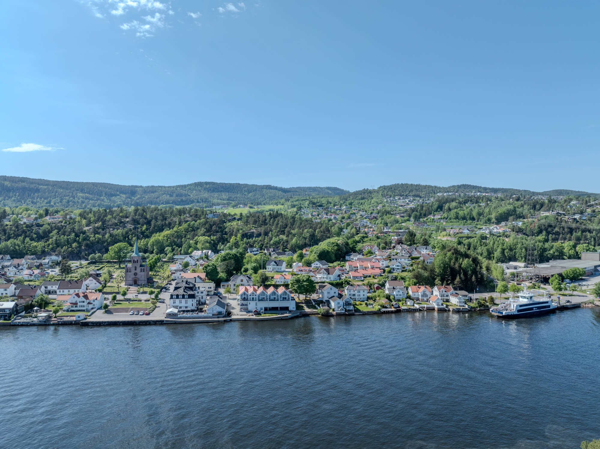 Buildings on both sides of a fjord where a ferry and other smaller boats are sailing