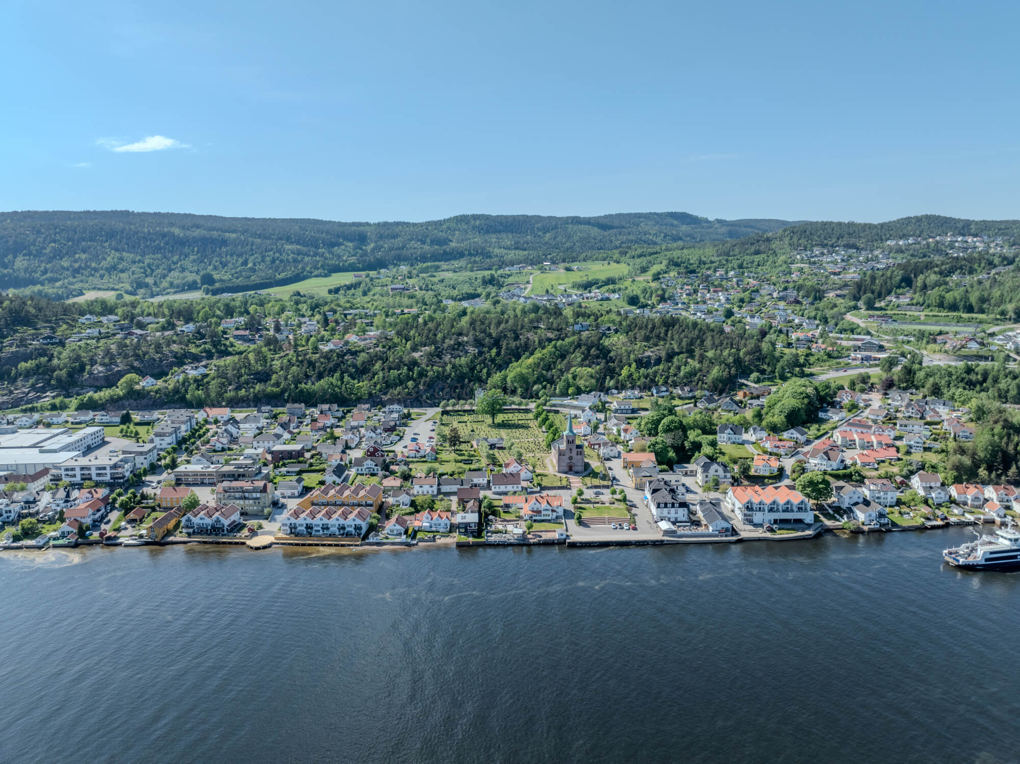 Buildings on both sides of a fjord where a ferry and other smaller boats are sailing