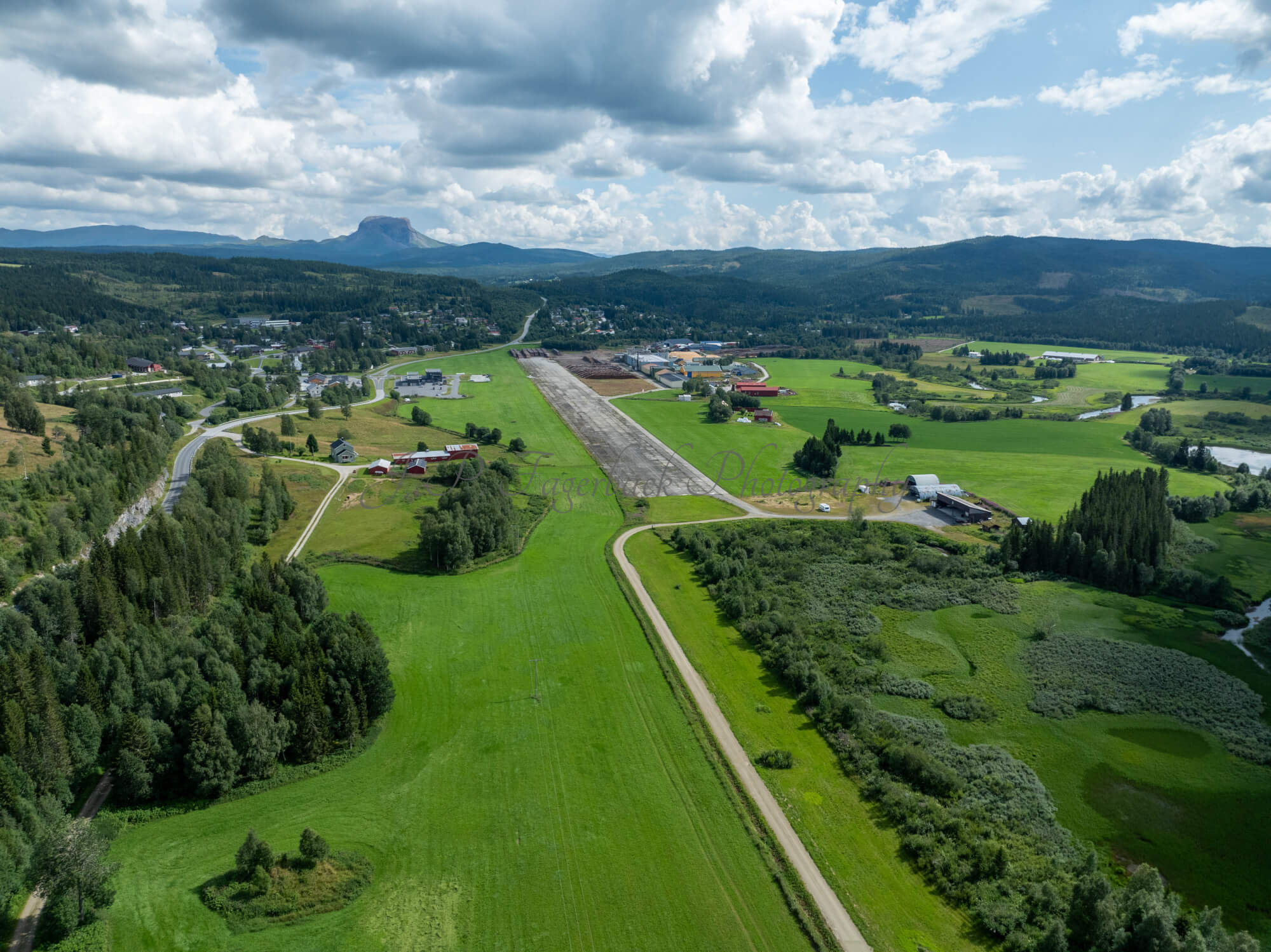 An old airstrip  and fields with buldings beyond it and mountains on the background where one looks like a hat