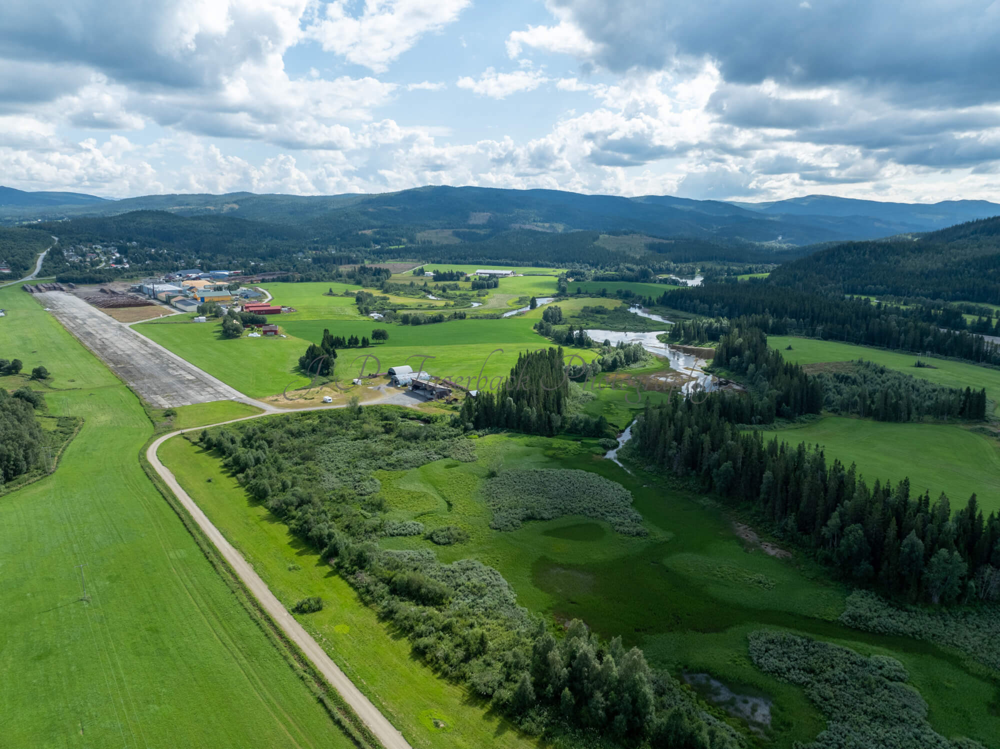 An old airstrip  and fields with buldings beyond it and mountains on the background where one looks like a hat