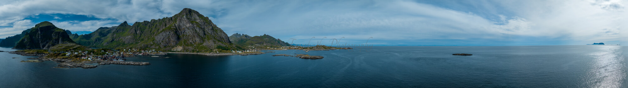 Buildings along the shore of a body of water with a mountain in the background on a gray day