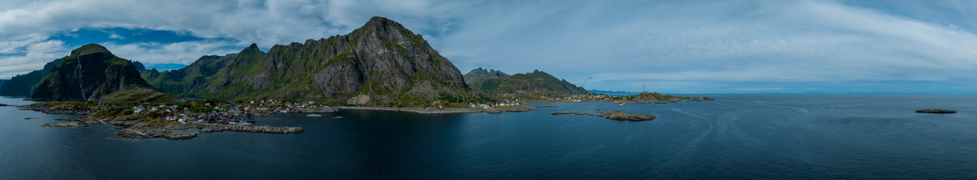 Buildings along the shore of a body of water with a mountain in the background on a gray day