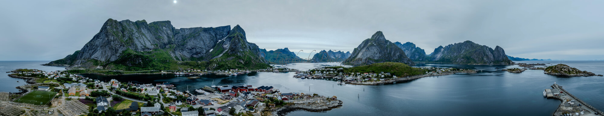 Buildings along the shore of a body of water with a mountain in the background on a gray day