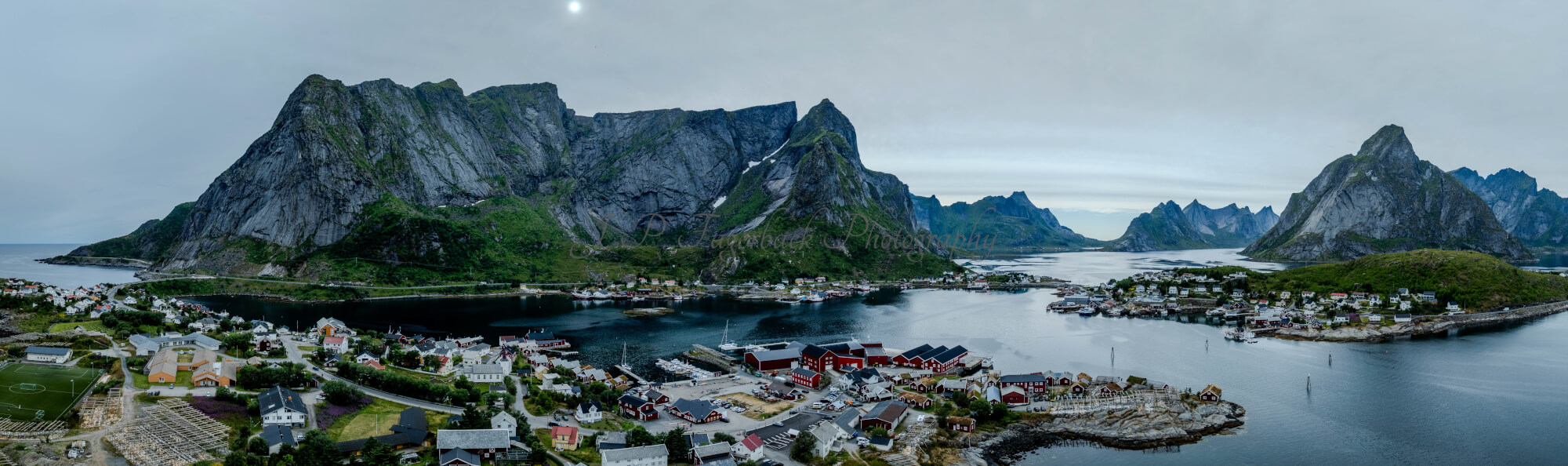 Buildings along the shore of a body of water with a mountain in the background on a gray day
