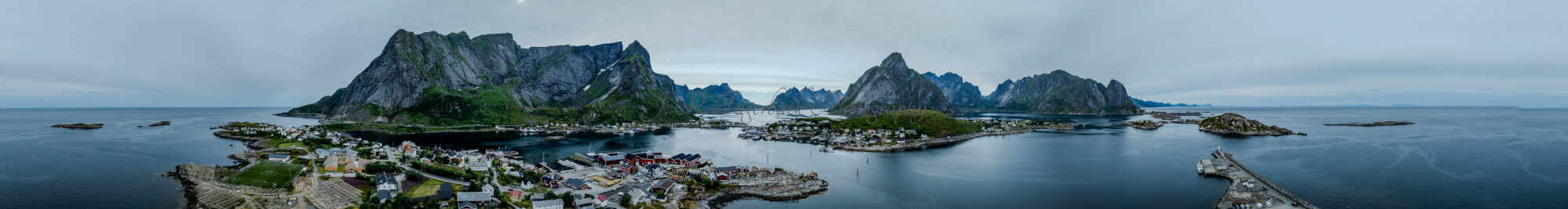 Buildings along the shore of a body of water with a mountain in the background on a gray day