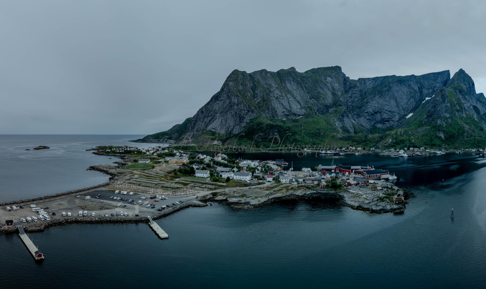 Buildings along the shore of a body of water with a mountain in the background on a gray day