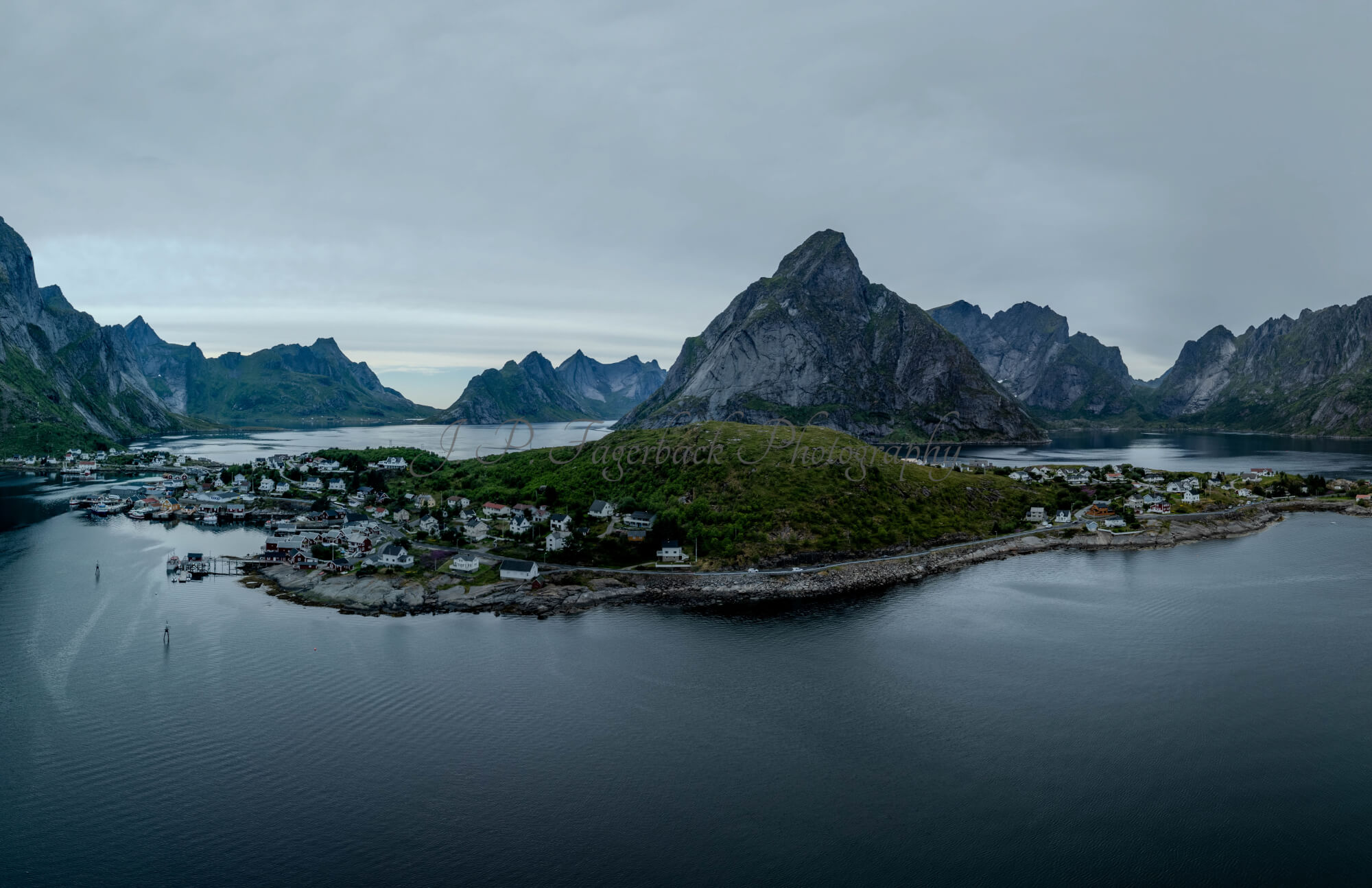 Buildings along the shore of a body of water with a mountain in the background on a gray day