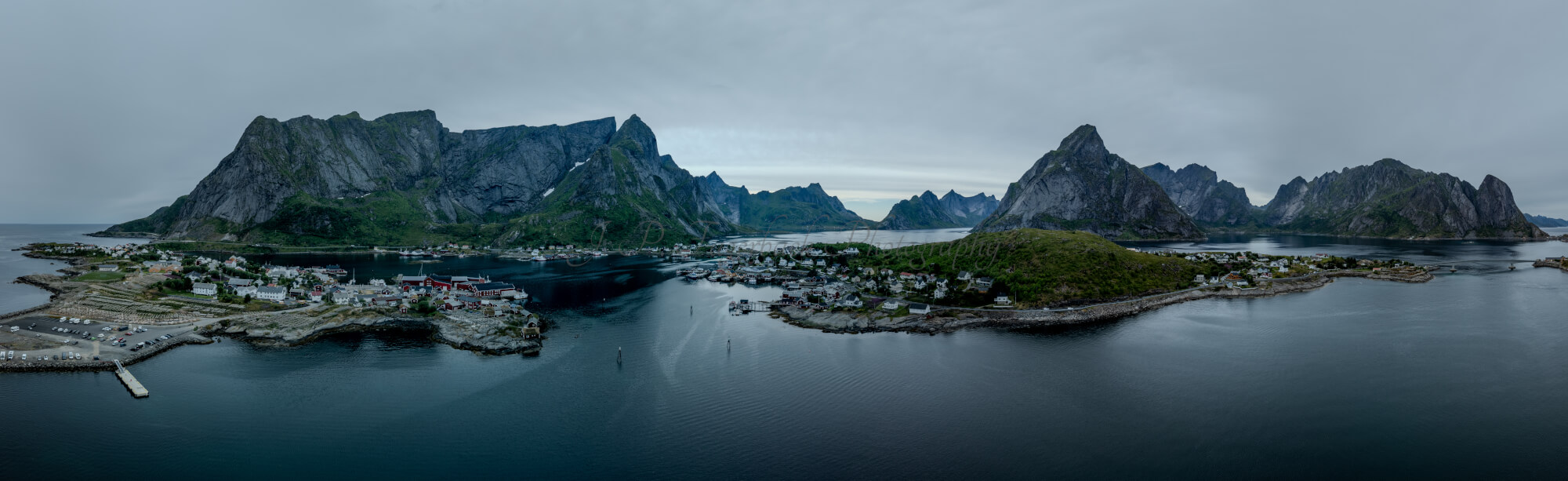 Buildings along the shore of a body of water with a mountain in the background on a gray day