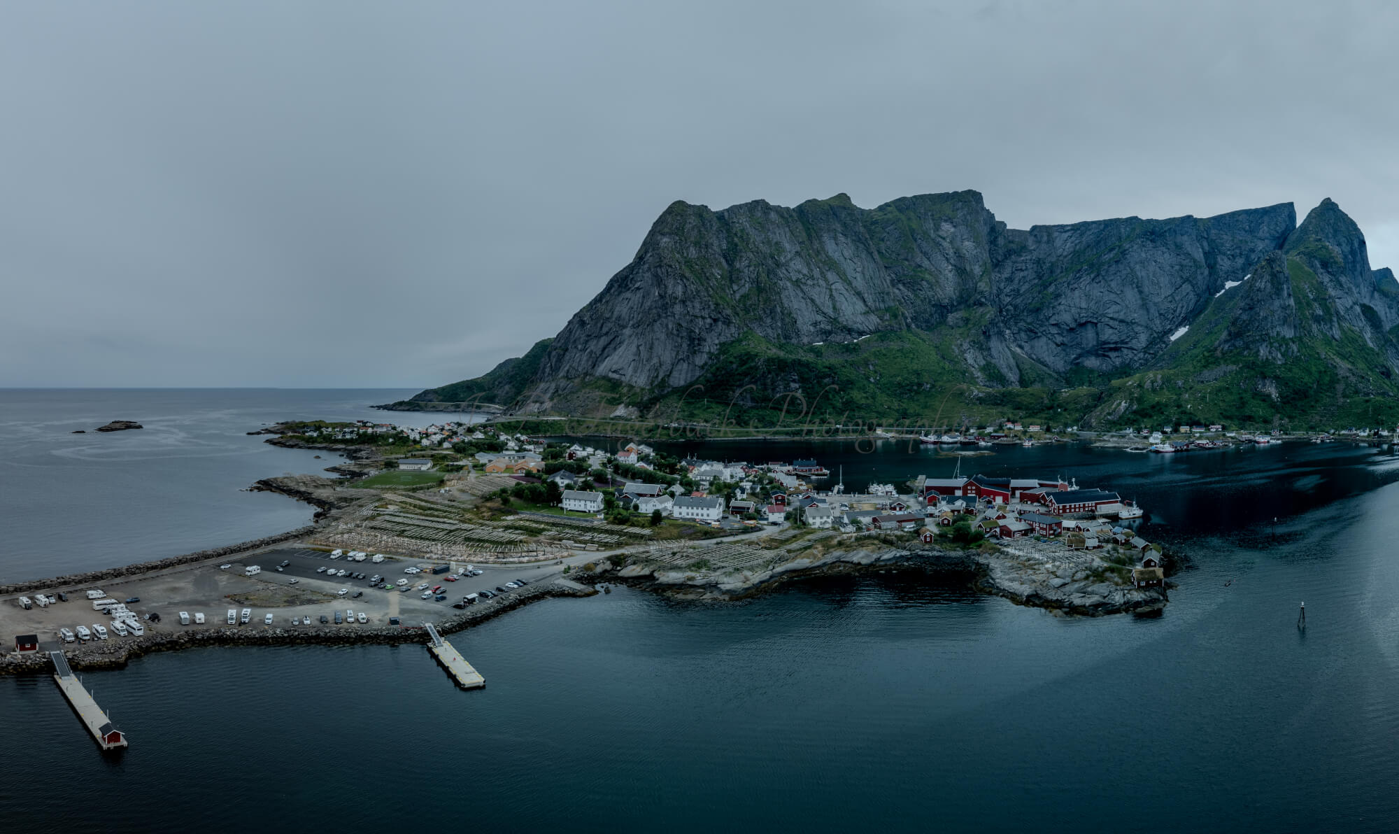 Buildings along the shore of a body of water with a mountain in the background on a gray day
