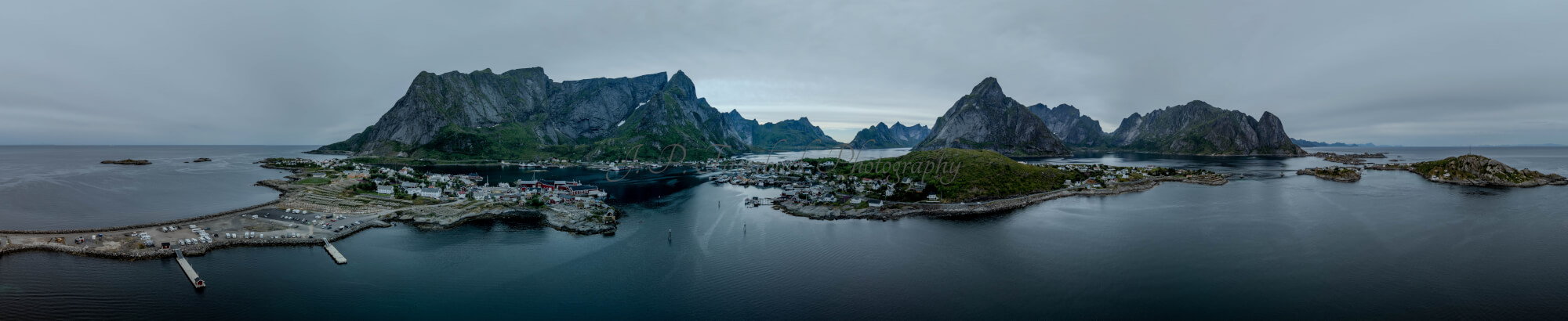 Buildings along the shore of a body of water with a mountain in the background on a gray day