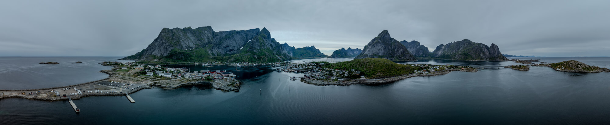 Buildings along the shore of a body of water with a mountain in the background on a gray day