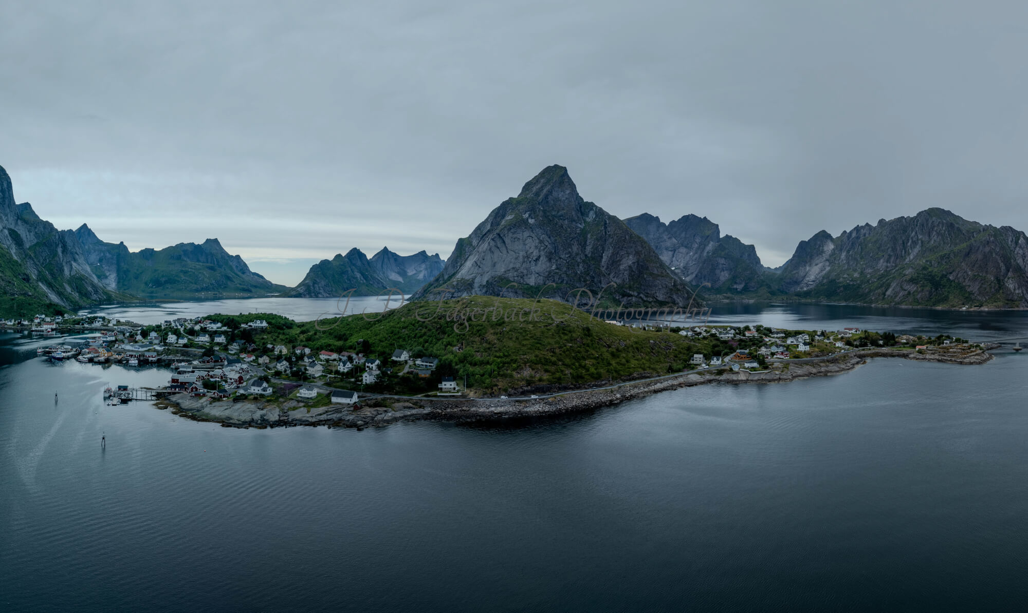 Buildings along the shore of a body of water with a mountain in the background on a gray day