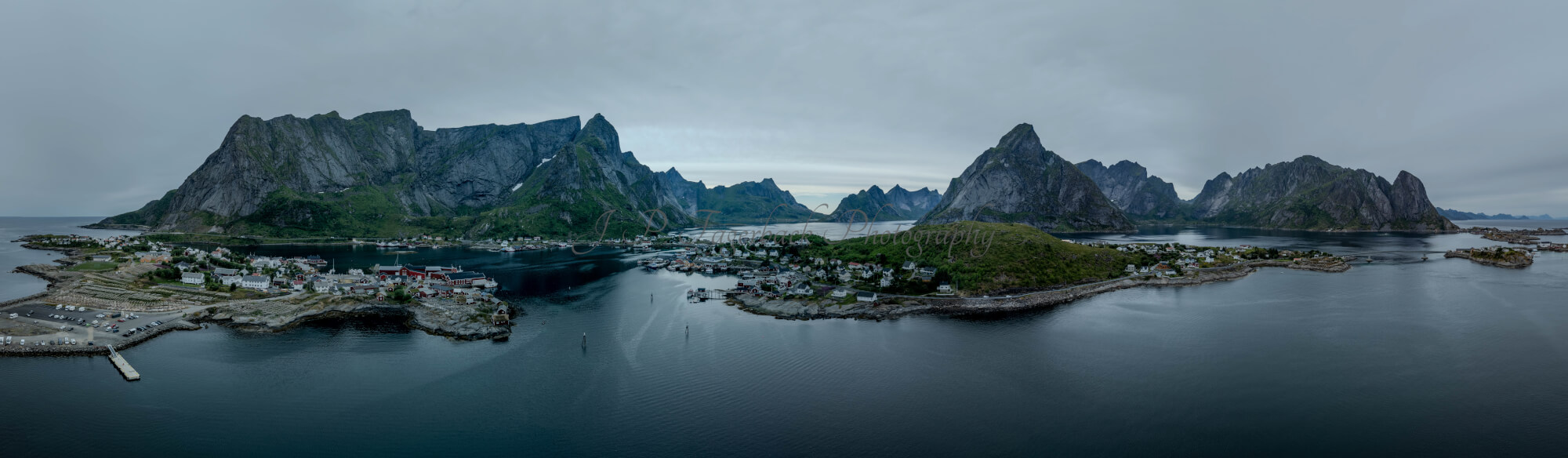 Buildings along the shore of a body of water with a mountain in the background on a gray day