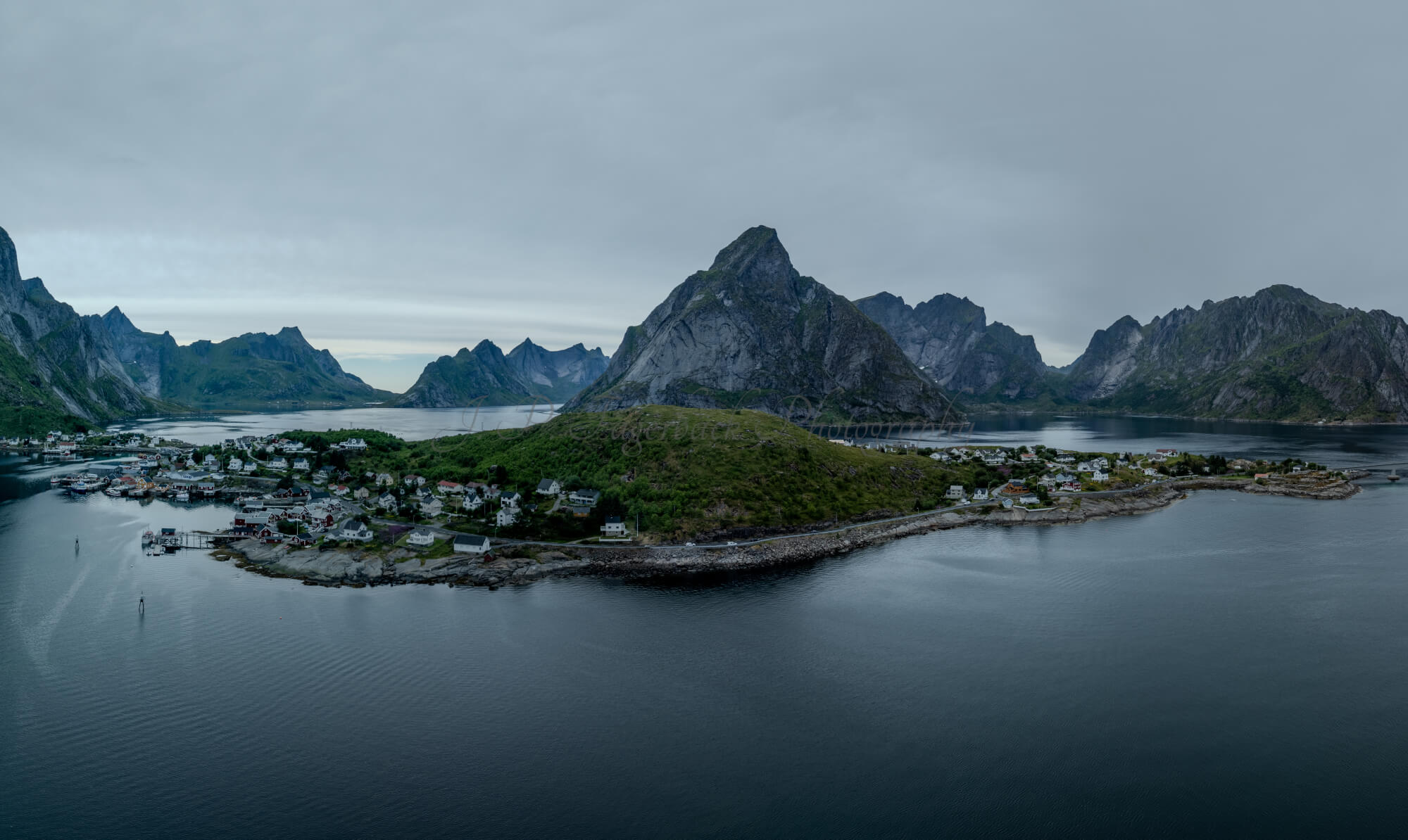 Buildings along the shore of a body of water with a mountain in the background on a gray day