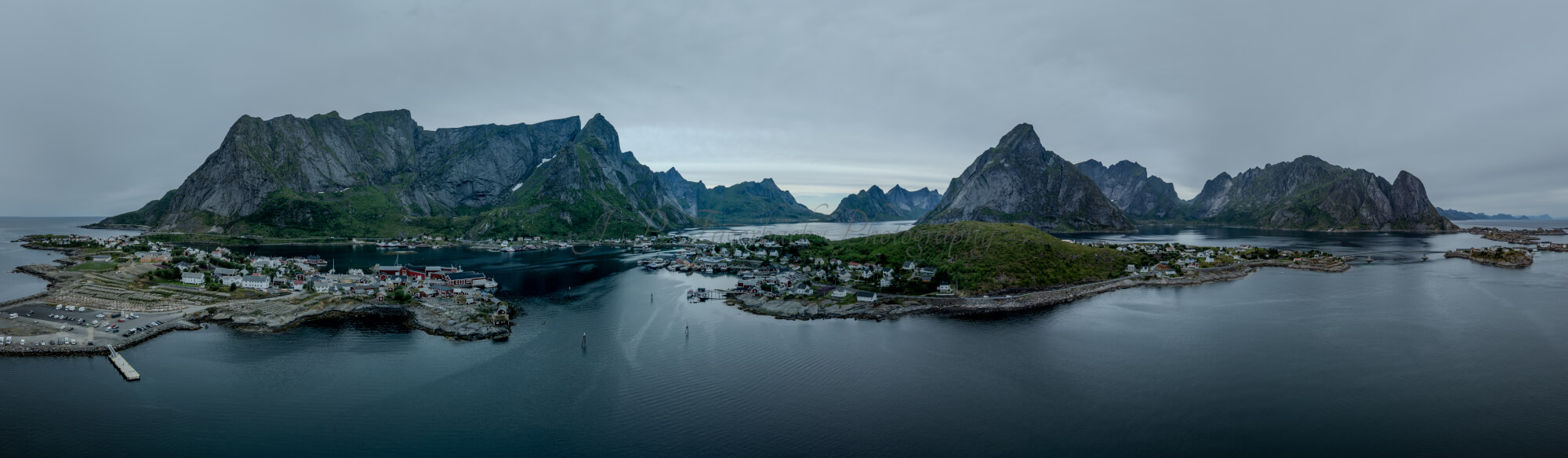 Buildings along the shore of a body of water with a mountain in the background on a gray day