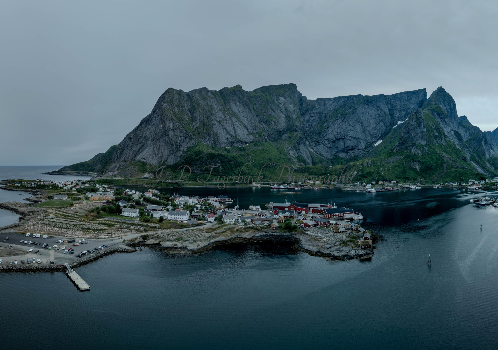 Buildings along the shore of a body of water with a mountain in the background on a gray day
