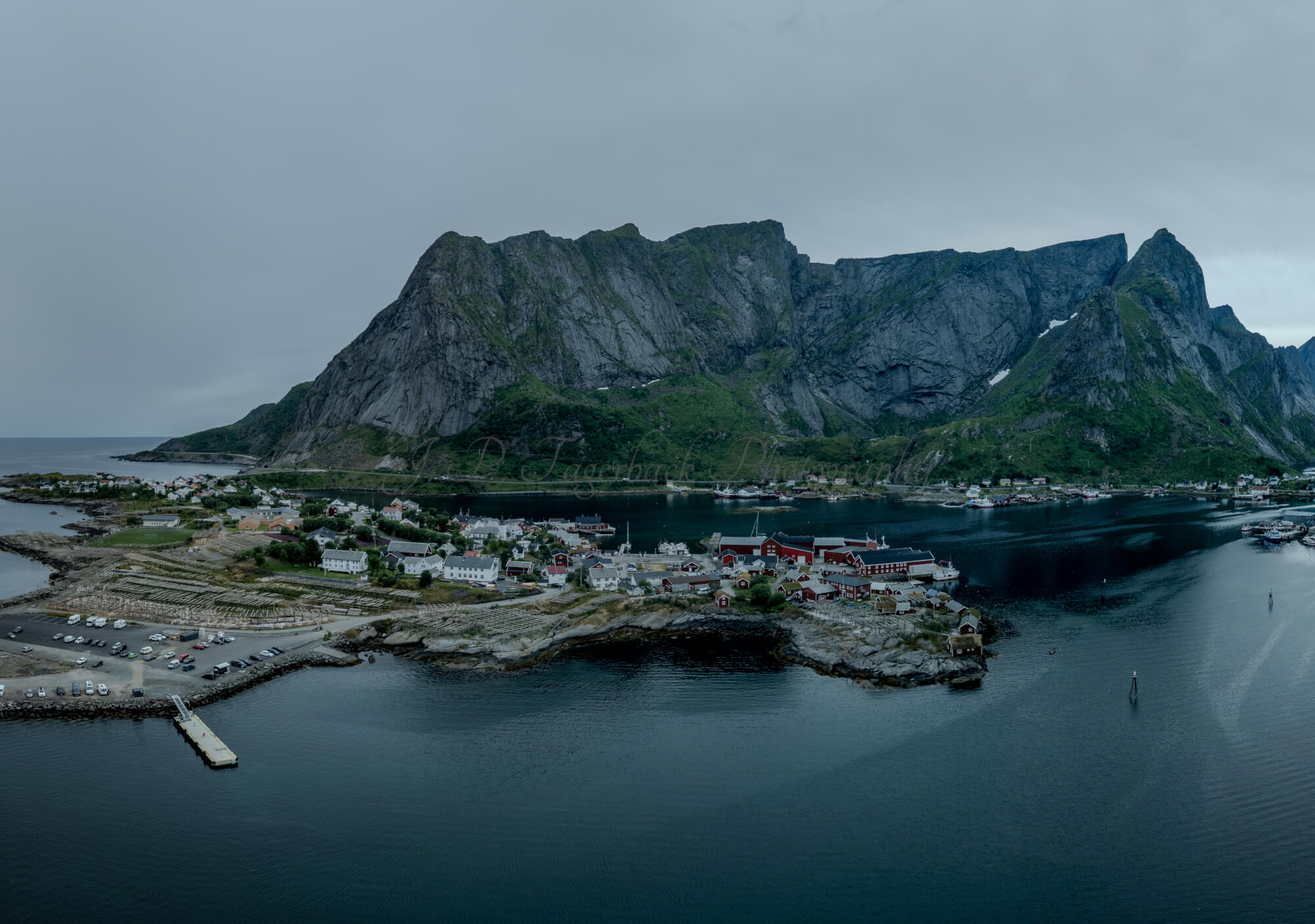 Buildings along the shore of a body of water with a mountain in the background on a gray day
