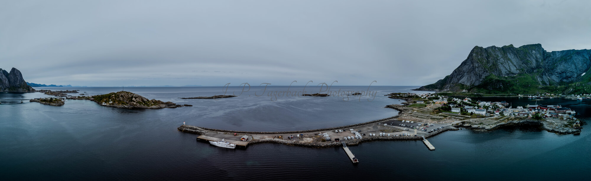 Buildings along the shore of a body of water with a mountain in the background on a gray day