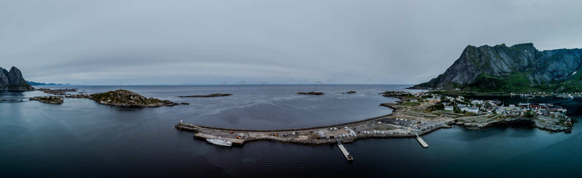 Buildings along the shore of a body of water with a mountain in the background on a gray day