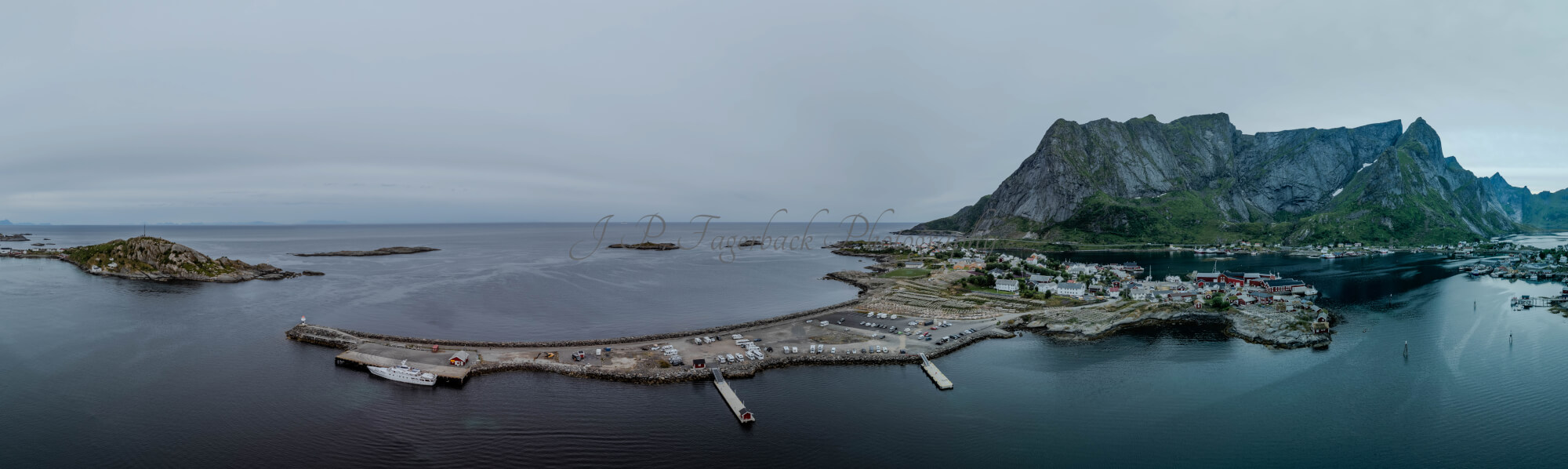 Buildings along the shore of a body of water with a mountain in the background on a gray day