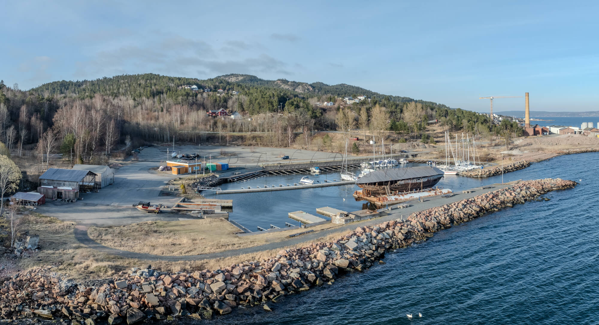An old ship  wreck with a protection roof over it in a marina by a large body of water under a blue sky